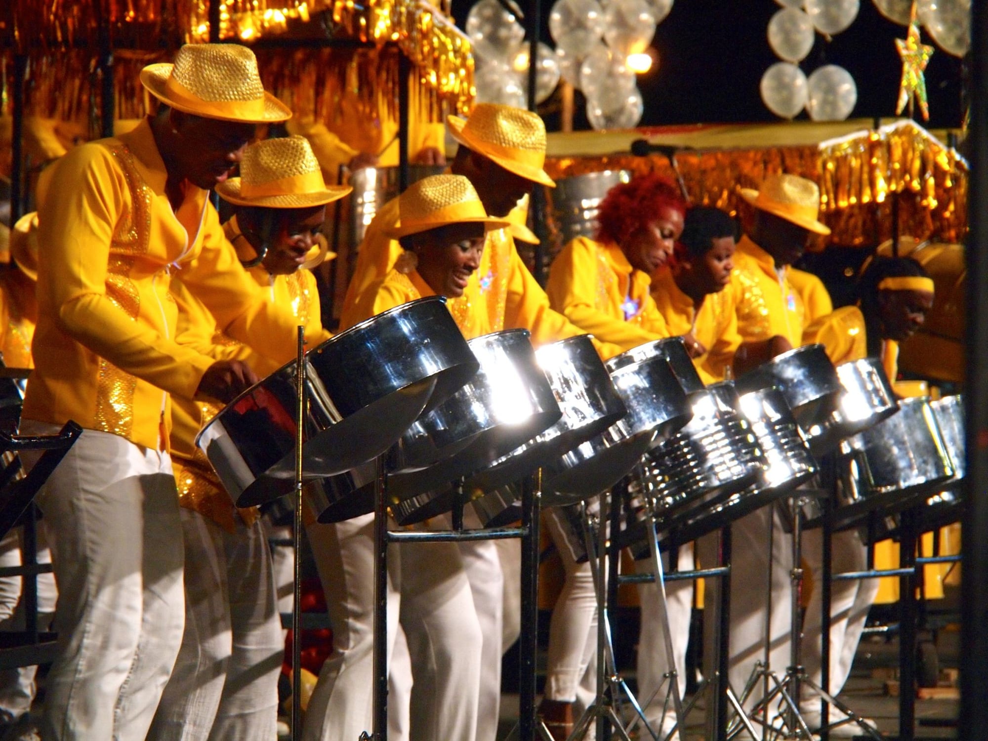 Rows of chrome steelpans mounted on stands, players in bright costumes performing at Carnival