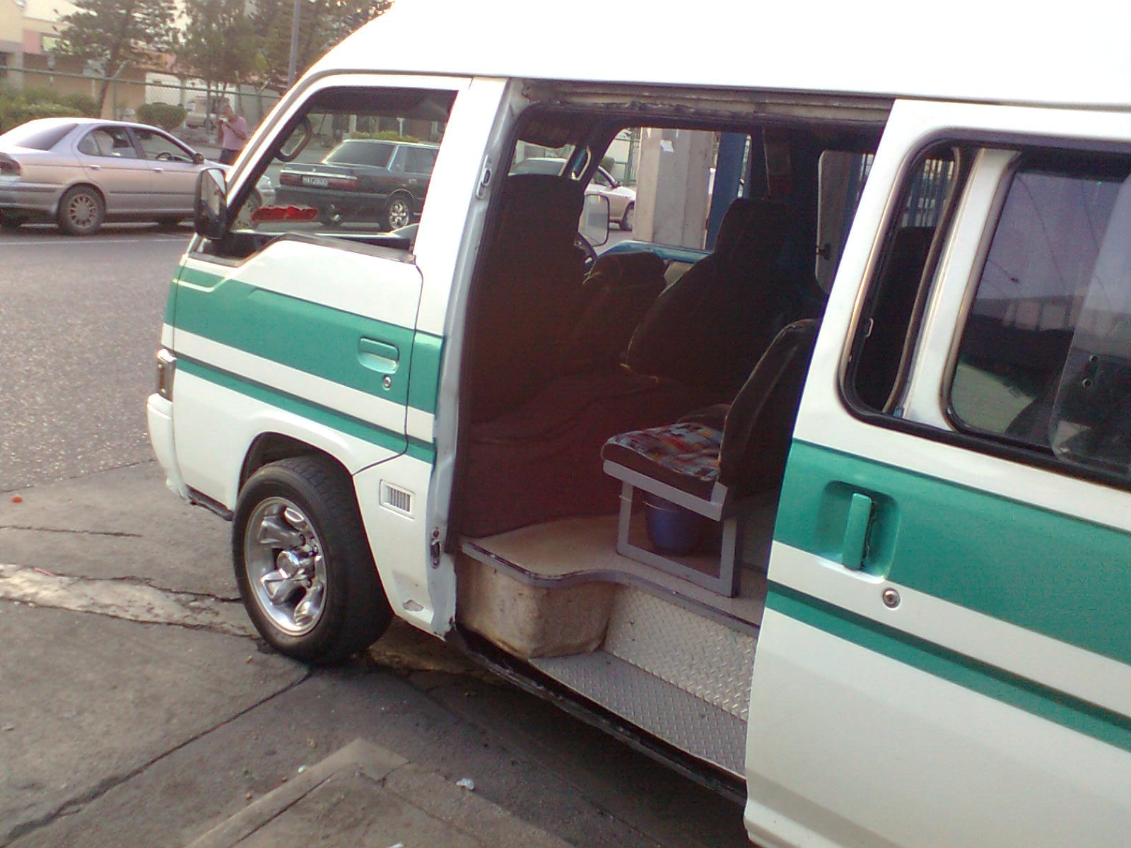 A white and green maxi-taxi minibus with its sliding door open, parked and waiting for passengers on a Trinidad street