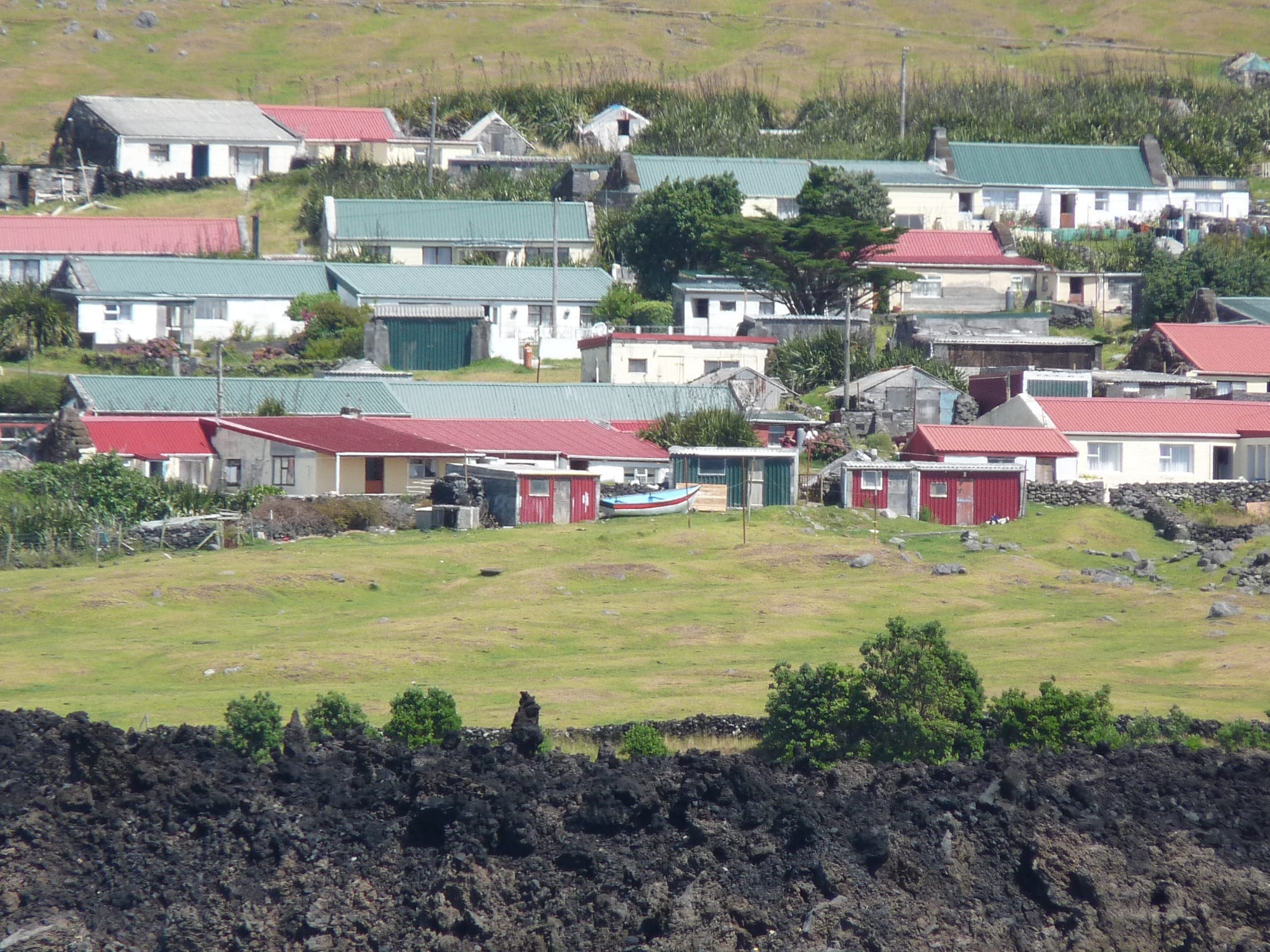 A small cluster of houses on a green coastal plain beneath steep hills