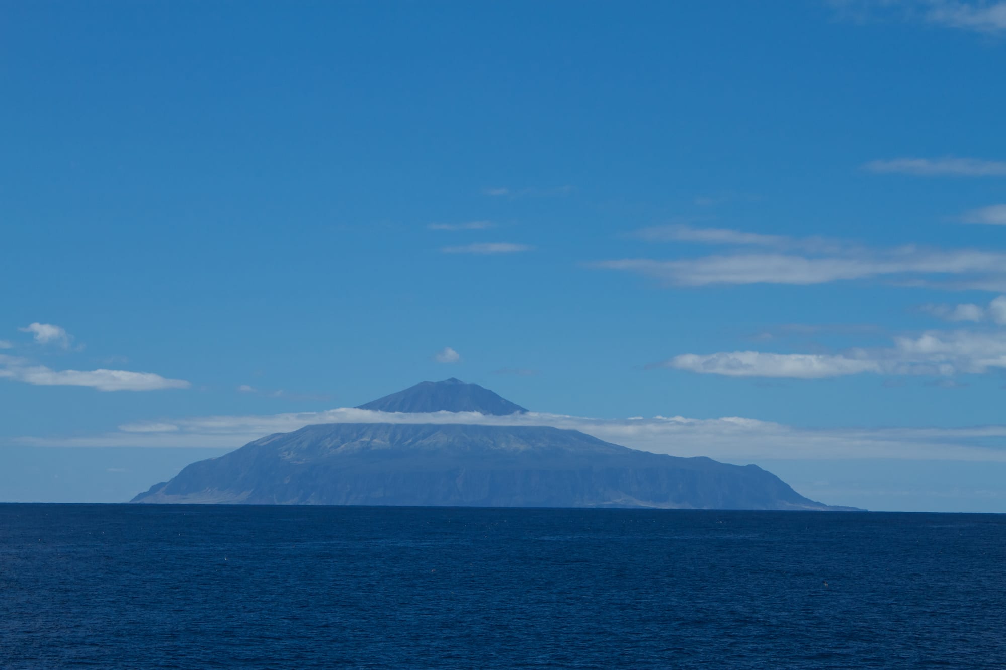 A steep volcanic island rising from the ocean, partly covered in cloud