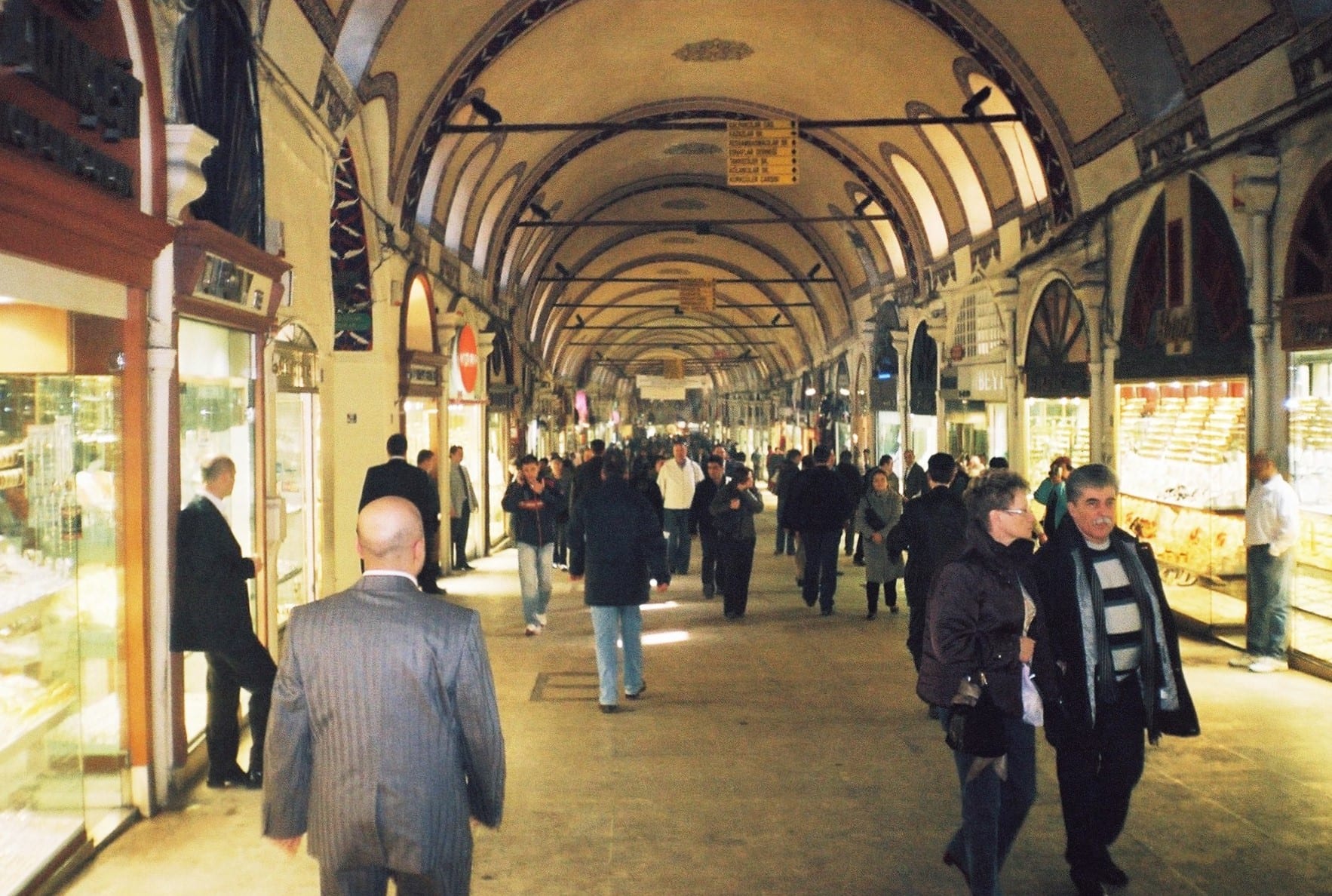 A covered, arched passageway of the Grand Bazaar in Istanbul, crowded with shoppers walking past jewellery and goods stalls