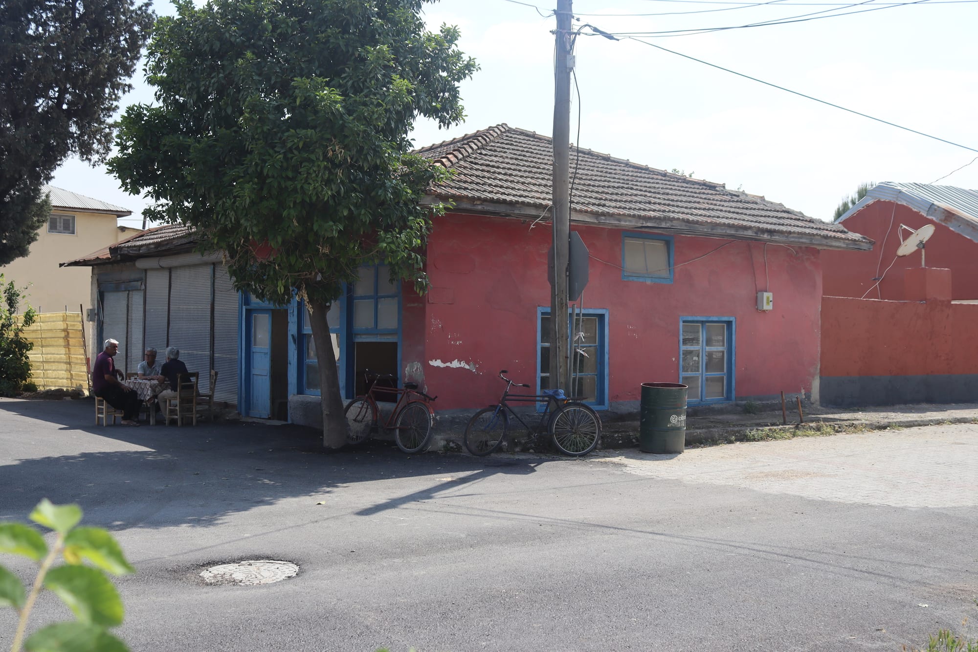 Three men sitting at a table outside a small village kahvehane, with bicycles parked against the wall