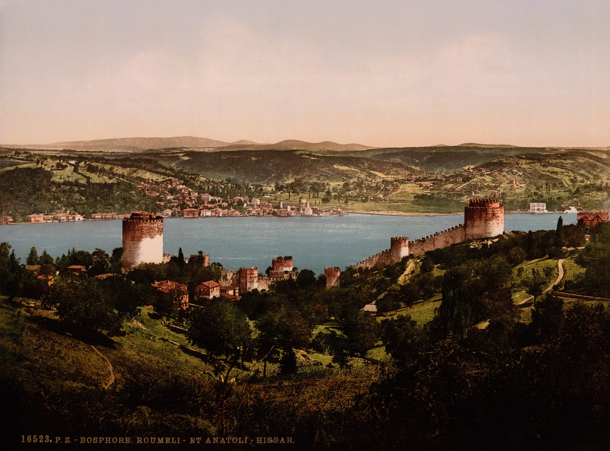 A hand-coloured 1890s view over the round stone towers and walls of a hillside fortress to the blue Bosphorus strait, with villages and hills on the far shore