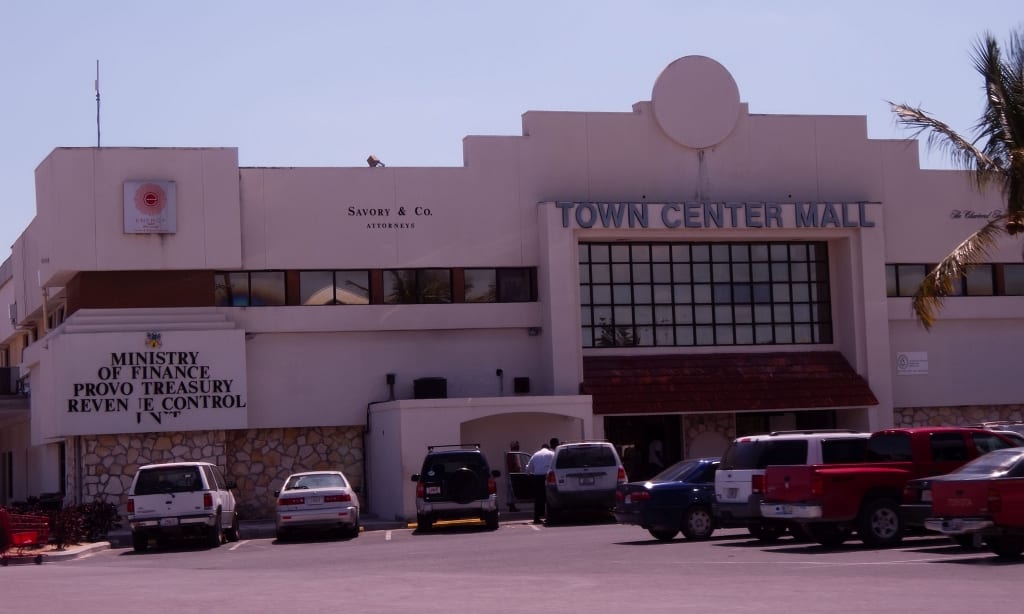 The cream-coloured Town Center Mall building on Providenciales, with the Ministry of Finance and Provo Treasury signage, palm trees and cars parked outside on a sunny day