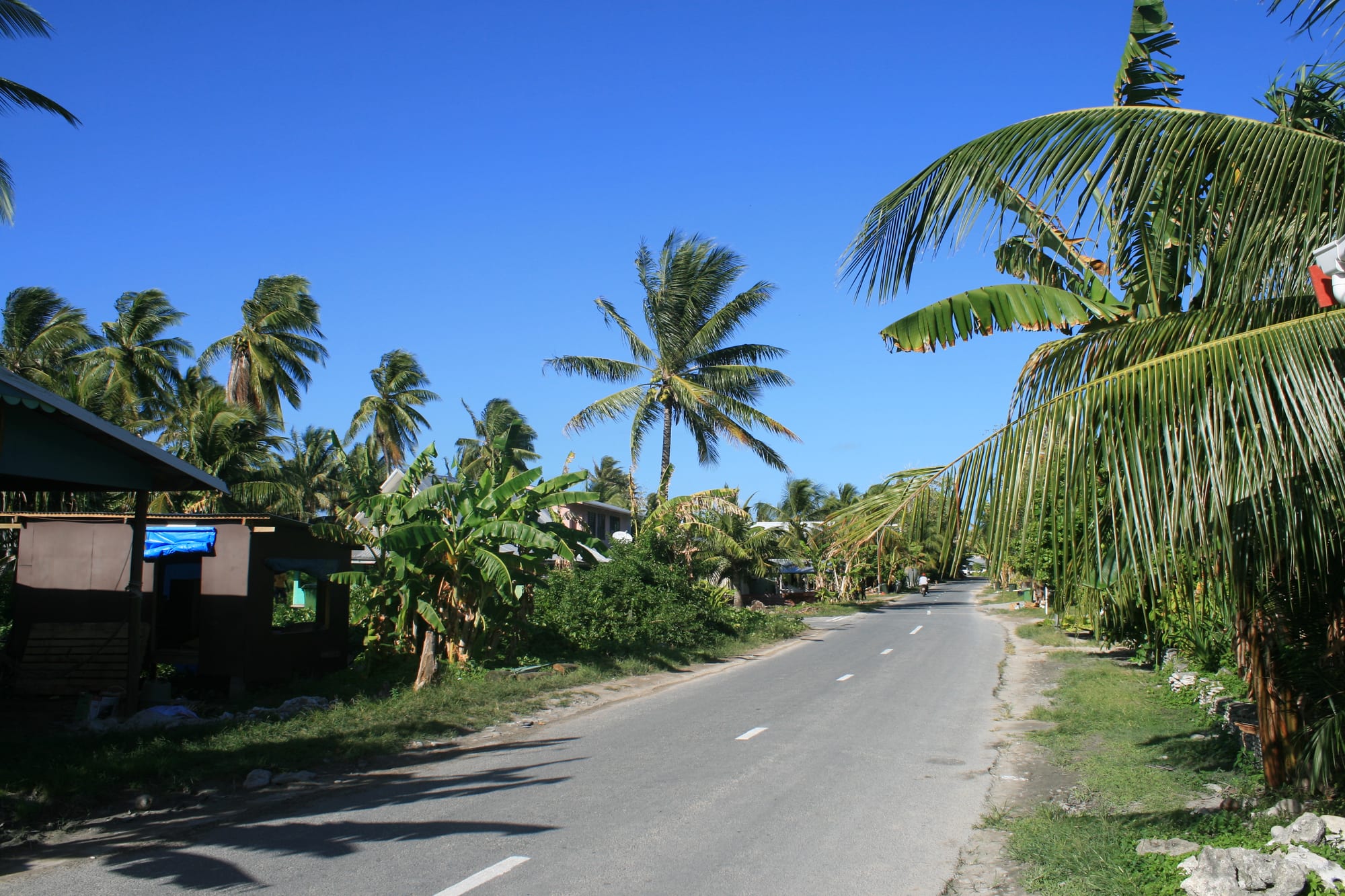 A narrow strip of coral atoll with buildings between the lagoon and open ocean