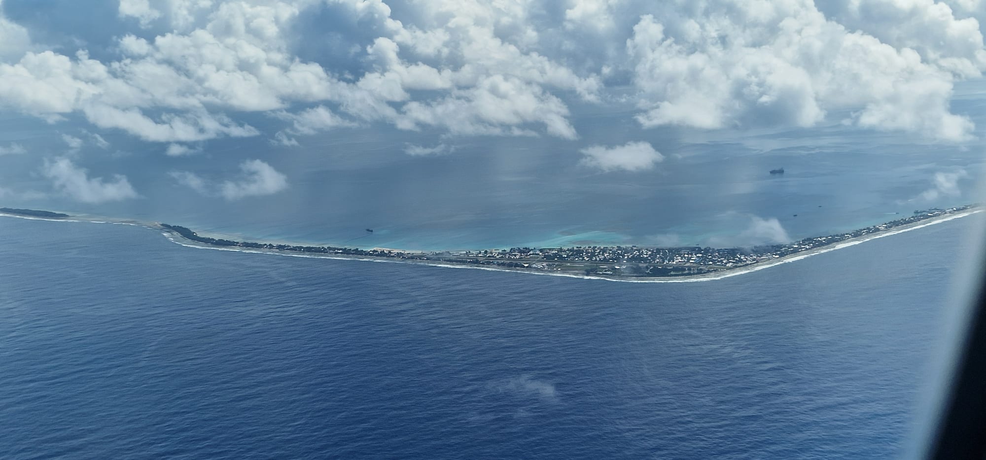 An aerial view of a narrow coral atoll surrounded by turquoise ocean