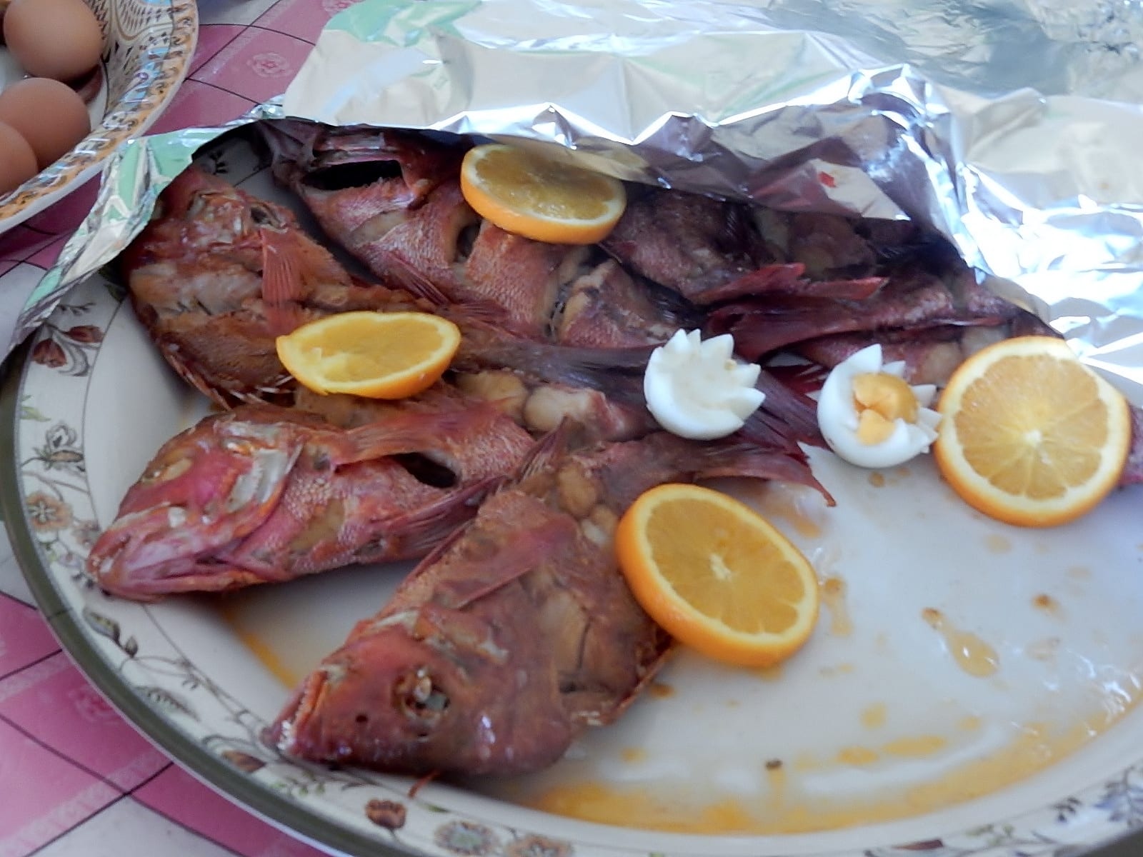 A plate of cooked whole fish garnished with orange slices