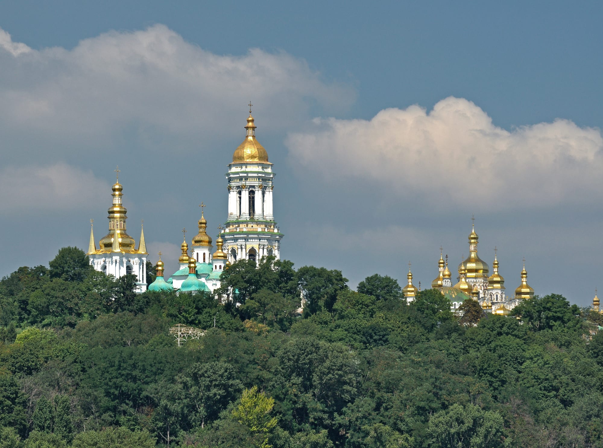 Gold and green onion domes rising above a wooded hilltop
