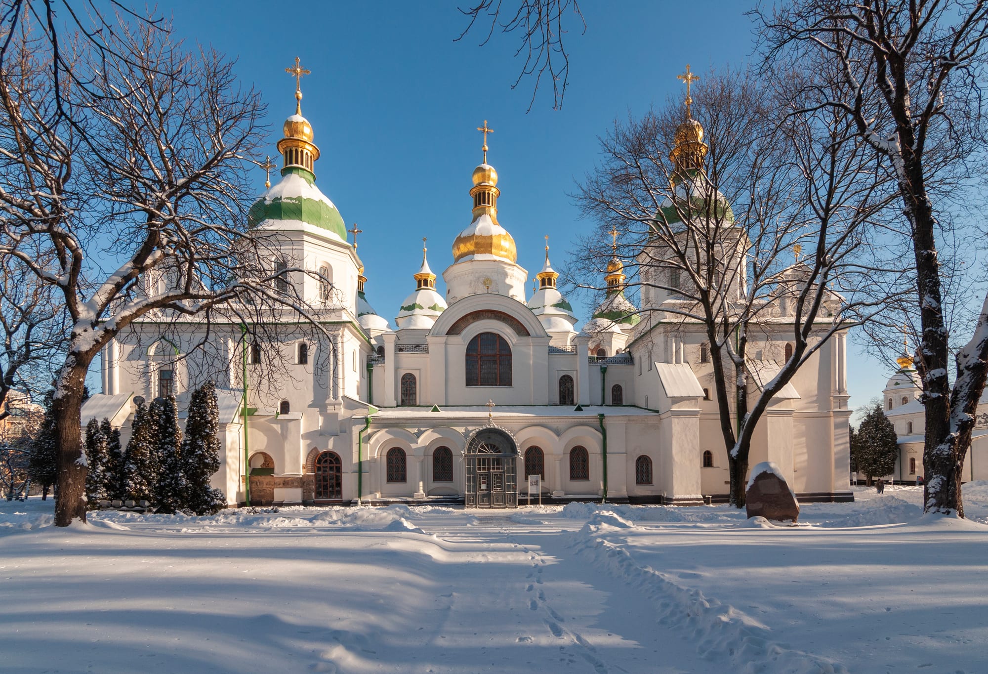 A white cathedral with golden and green domes, seen in winter snow