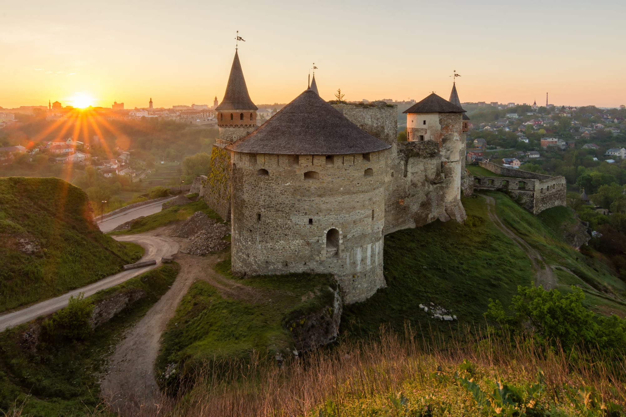 A stone medieval fortress with round towers on a hilltop at sunrise