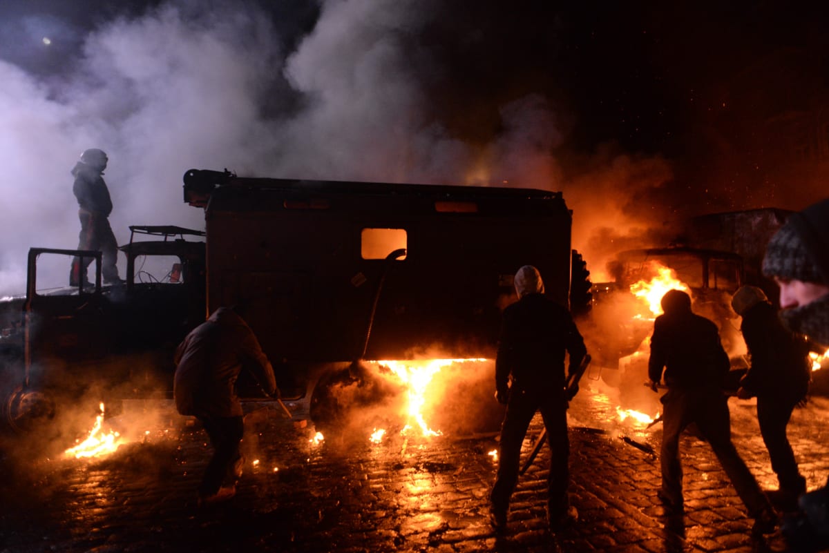 Protesters behind burning barricades sending up thick black smoke on a Kyiv street at night, January 2014