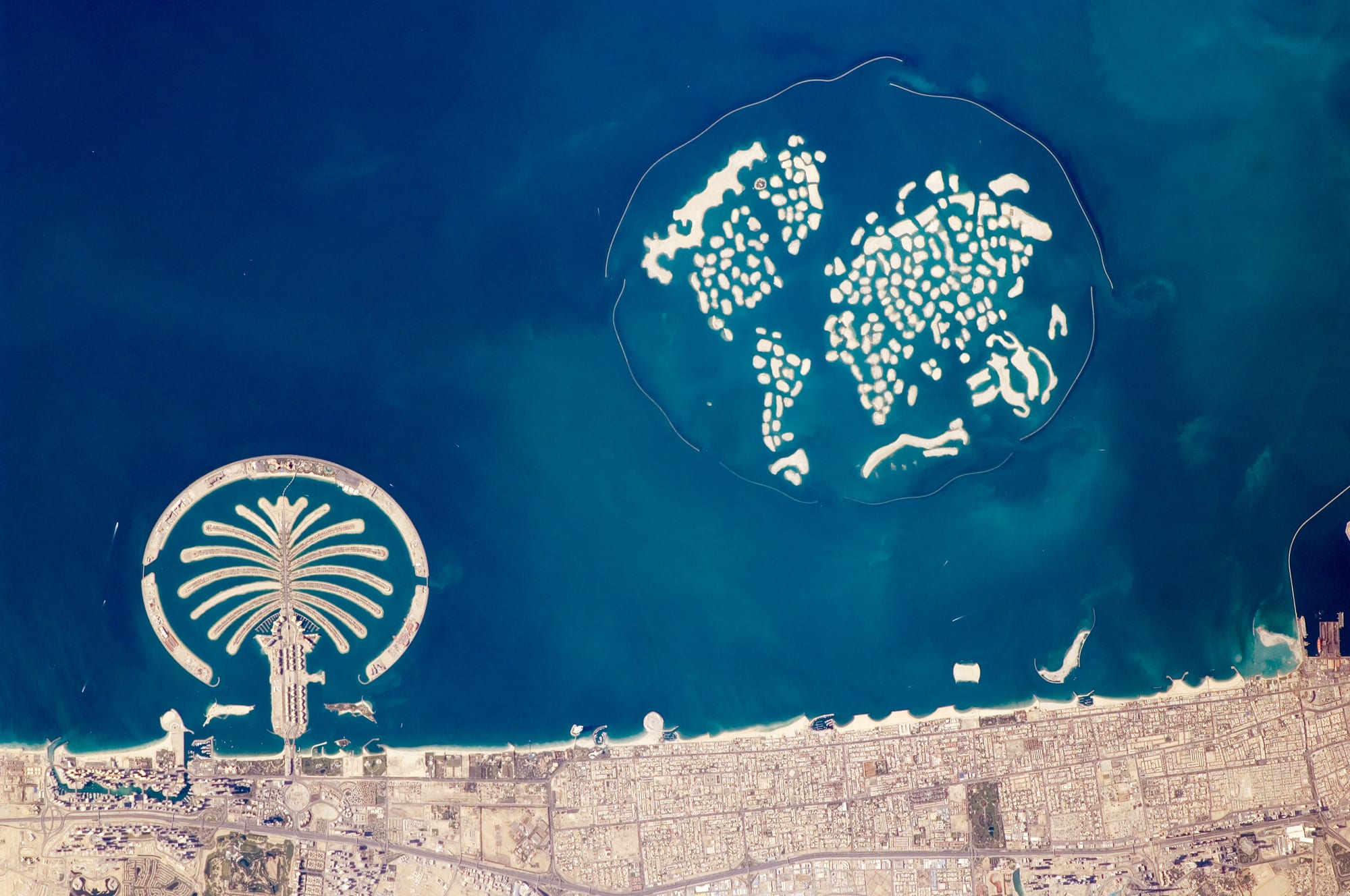 A satellite view of artificial palm-shaped islands off a coastal city