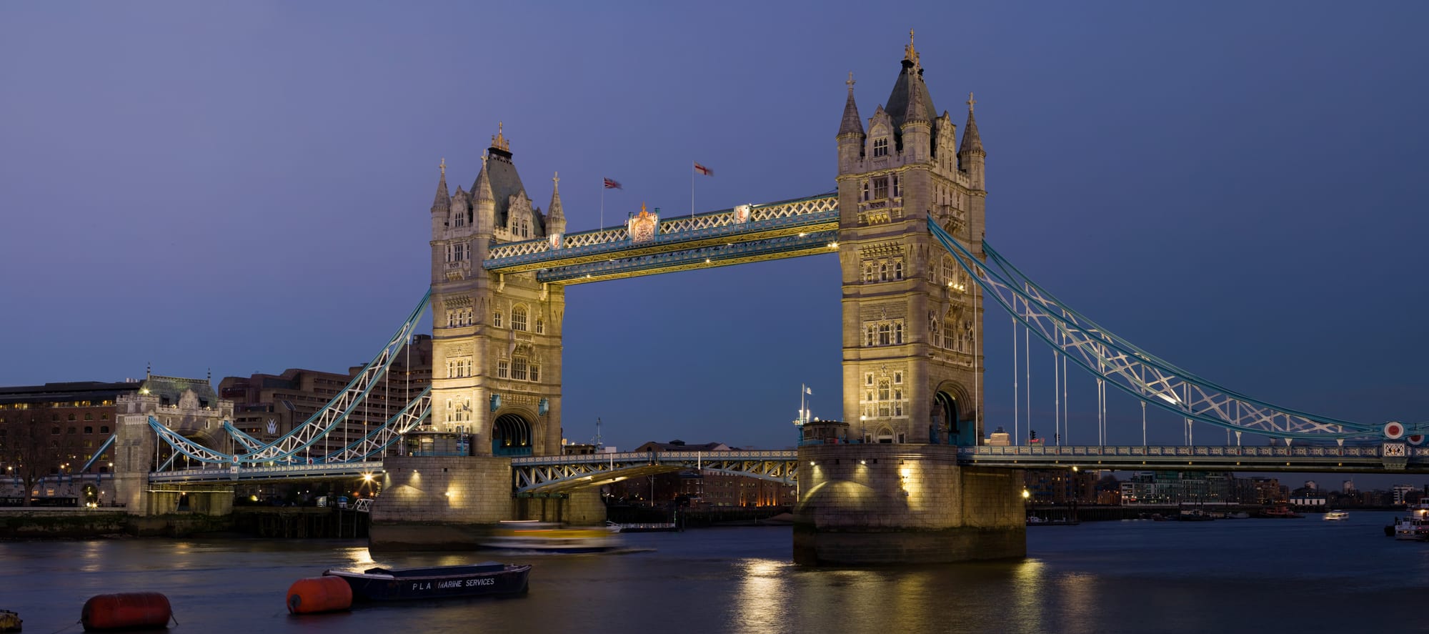 An ornate Victorian bridge with twin towers over a river at dusk
