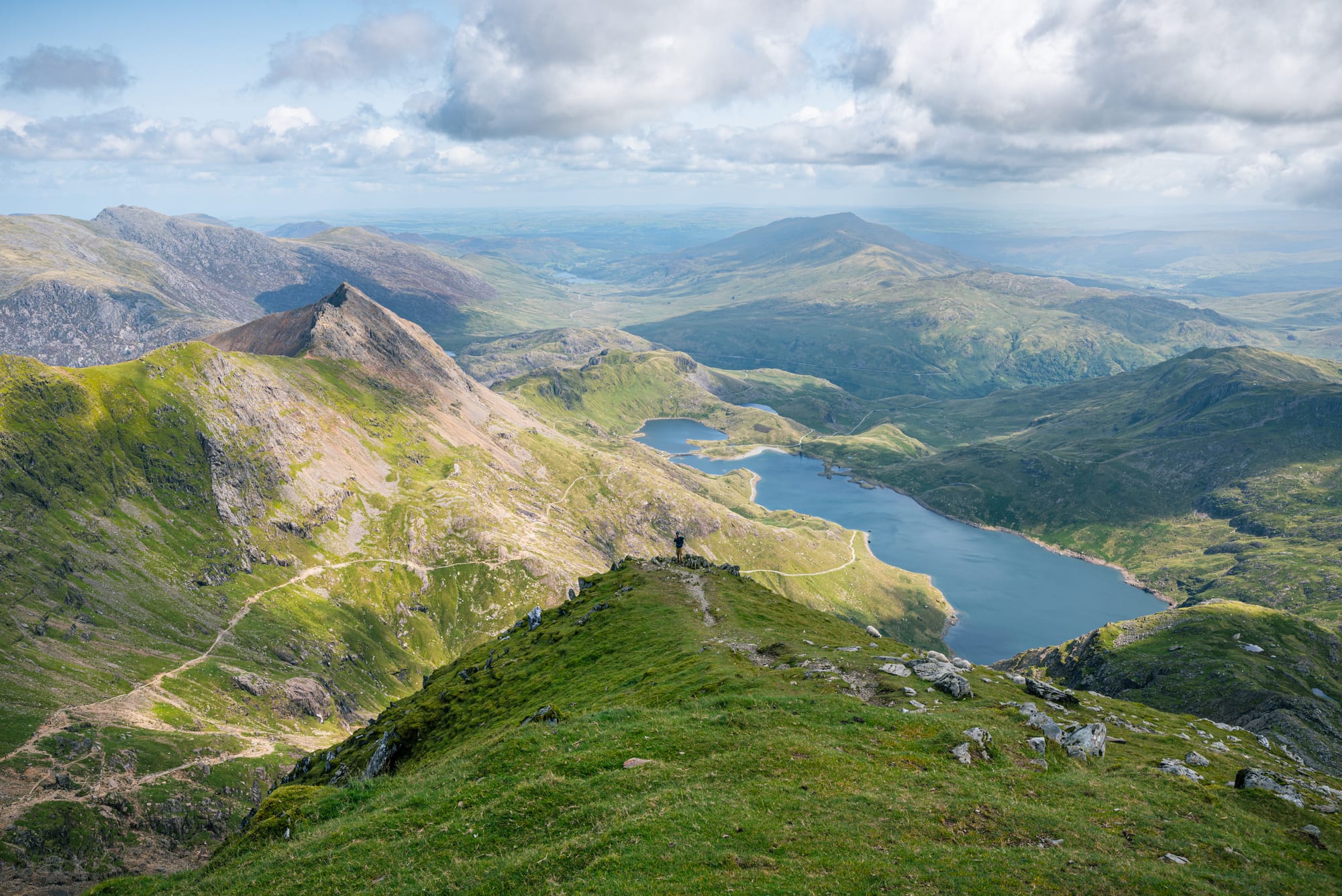 A hiker on a mountain ridge overlooking a lake and jagged peaks