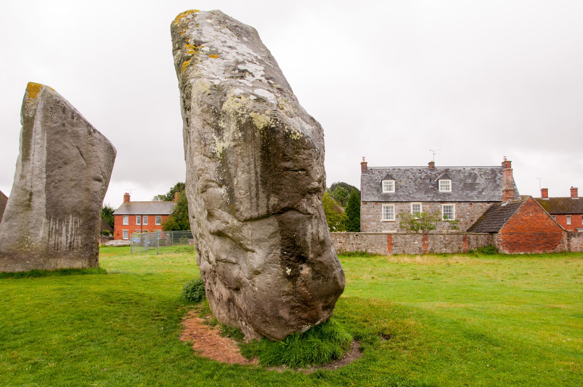 Massive weathered standing stones on grass, with a village of houses built within the ancient monument