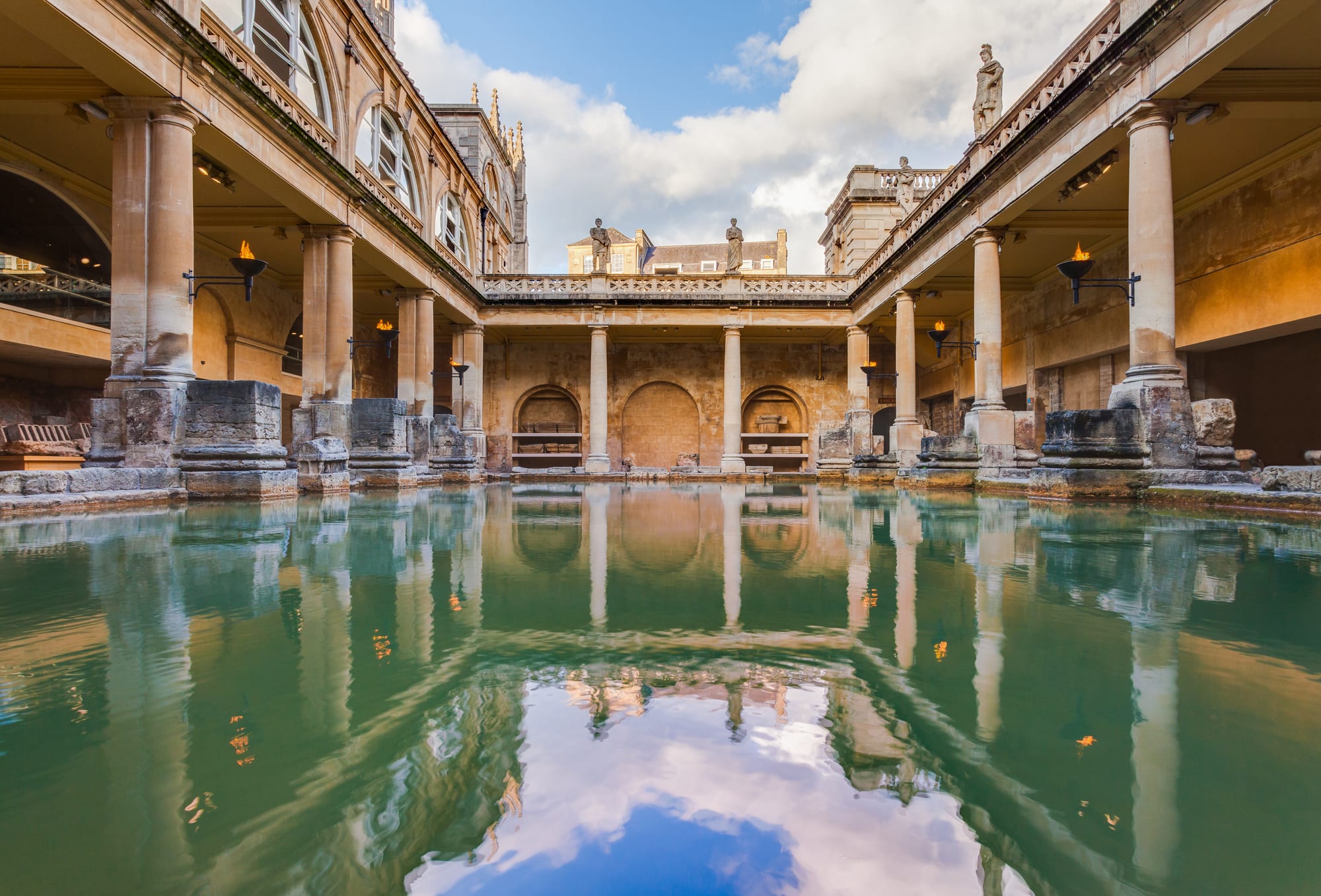 A steaming green pool surrounded by Roman columns and statues