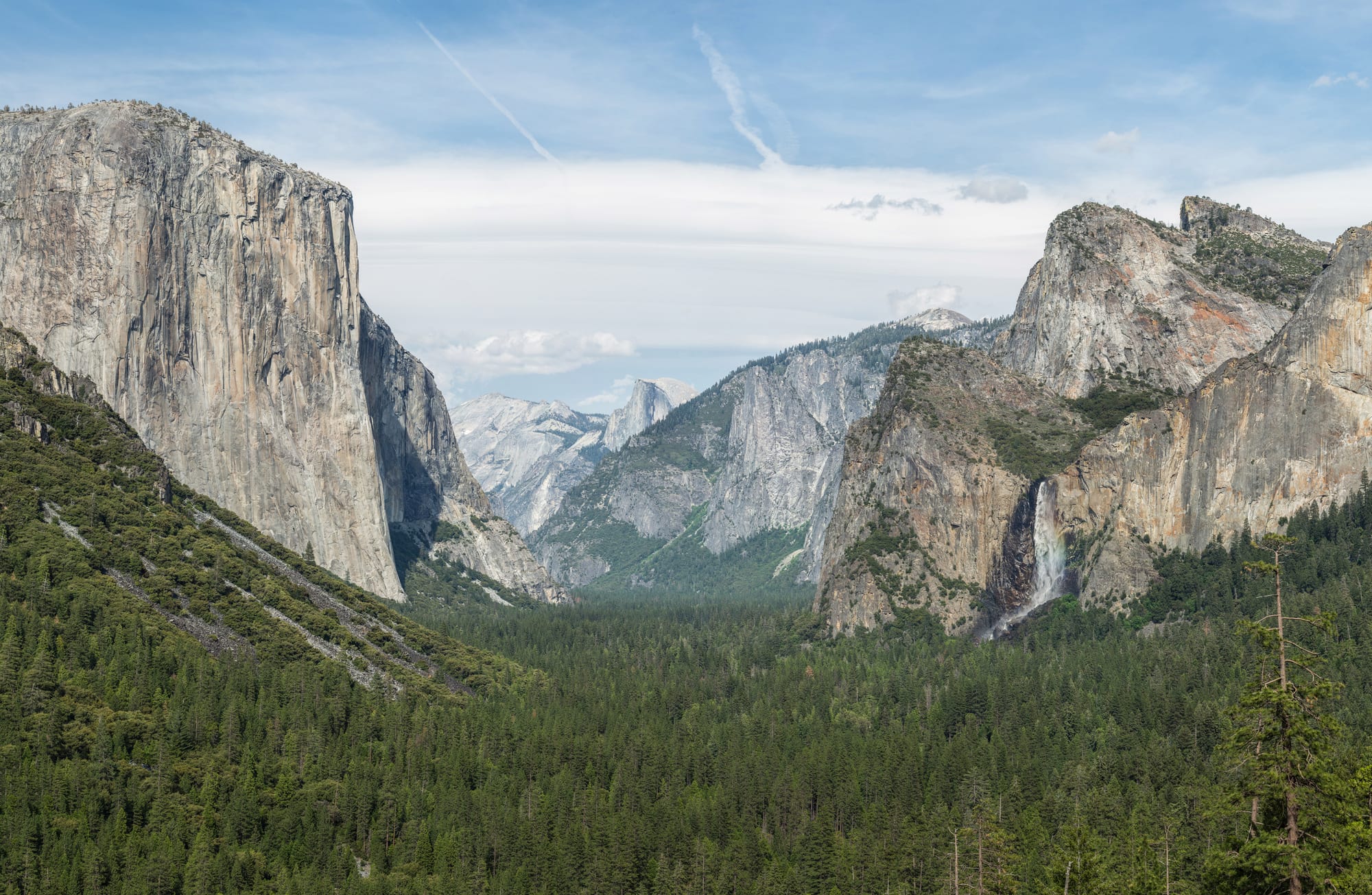 A granite valley with sheer cliffs, a waterfall, and a distant domed peak