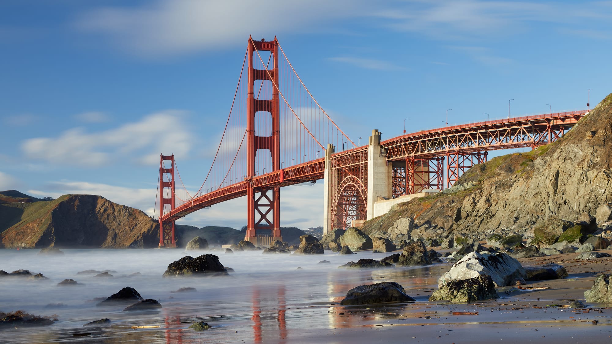A large orange suspension bridge spanning a strait, partly wrapped in fog