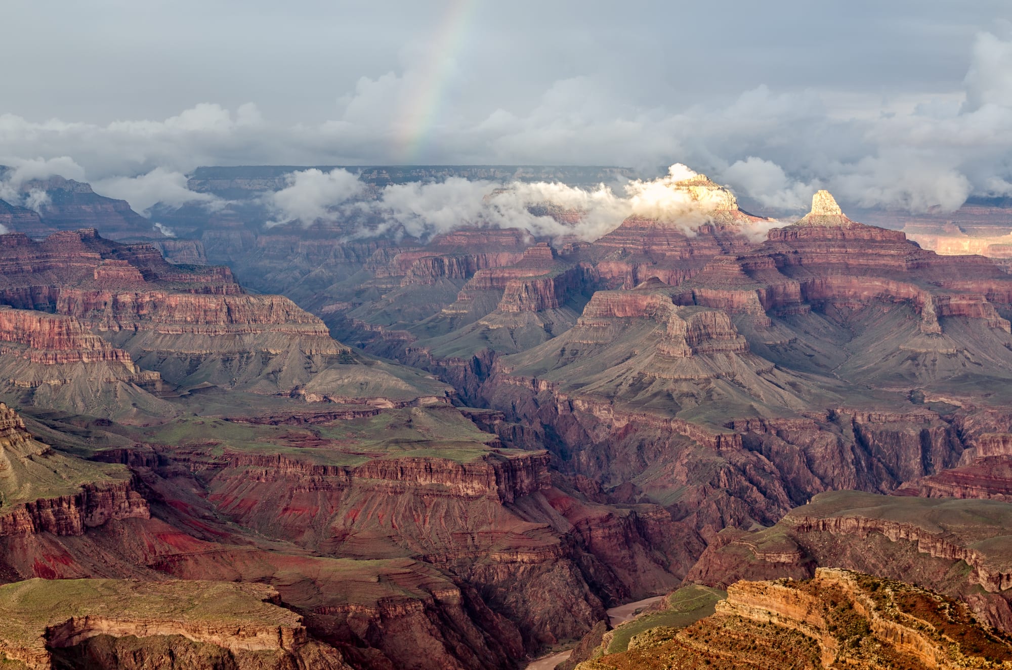 A rainbow arcing over a vast, layered canyon landscape