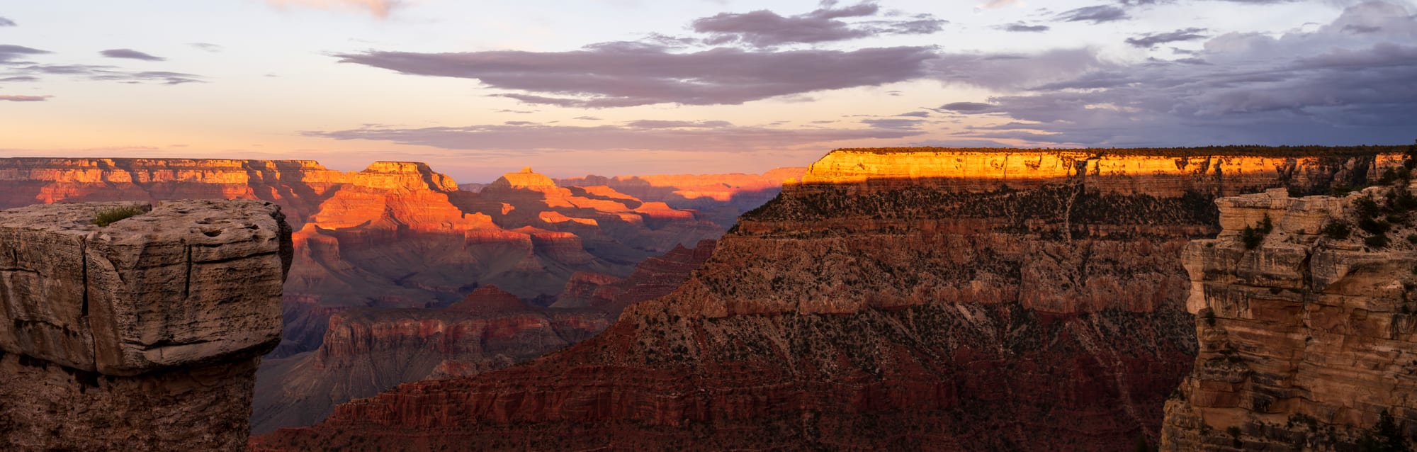 A vast canyon with layered red rock walls under a sunset sky