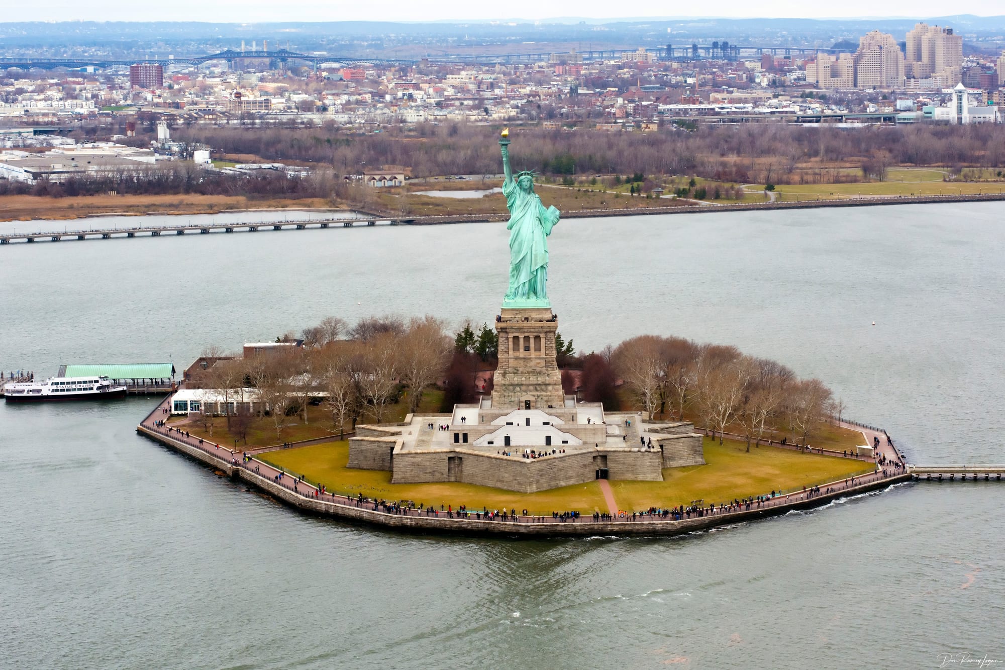 A large green statue of a robed woman holding a torch, on an island in a harbour
