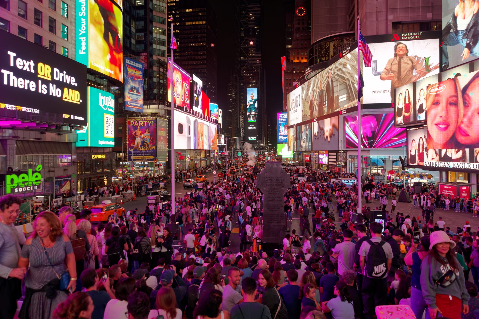A busy urban square filled with enormous illuminated billboards