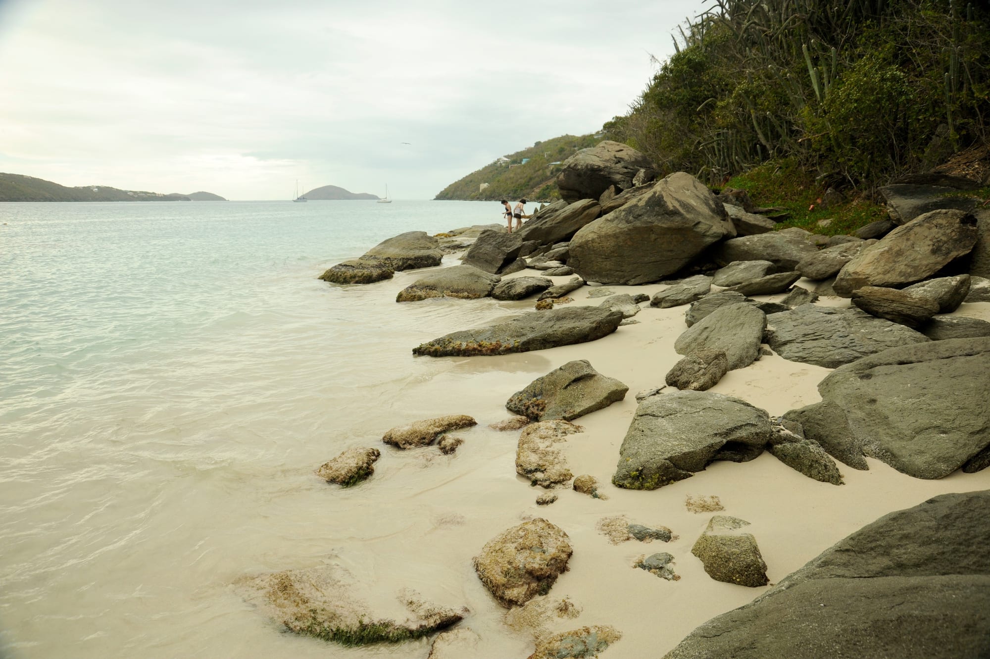 A curved white sand beach along a calm turquoise bay surrounded by green hills