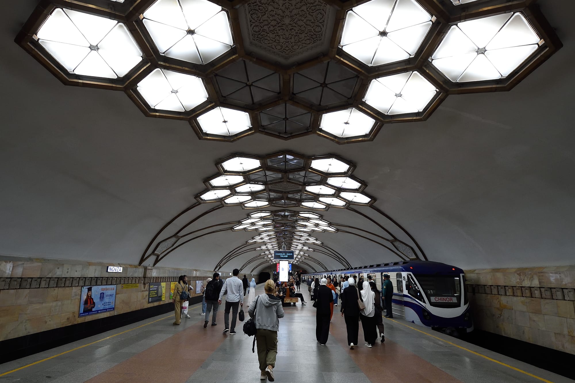 Passengers walking along the platform of an ornately decorated Tashkent Metro station as a train waits at the platform