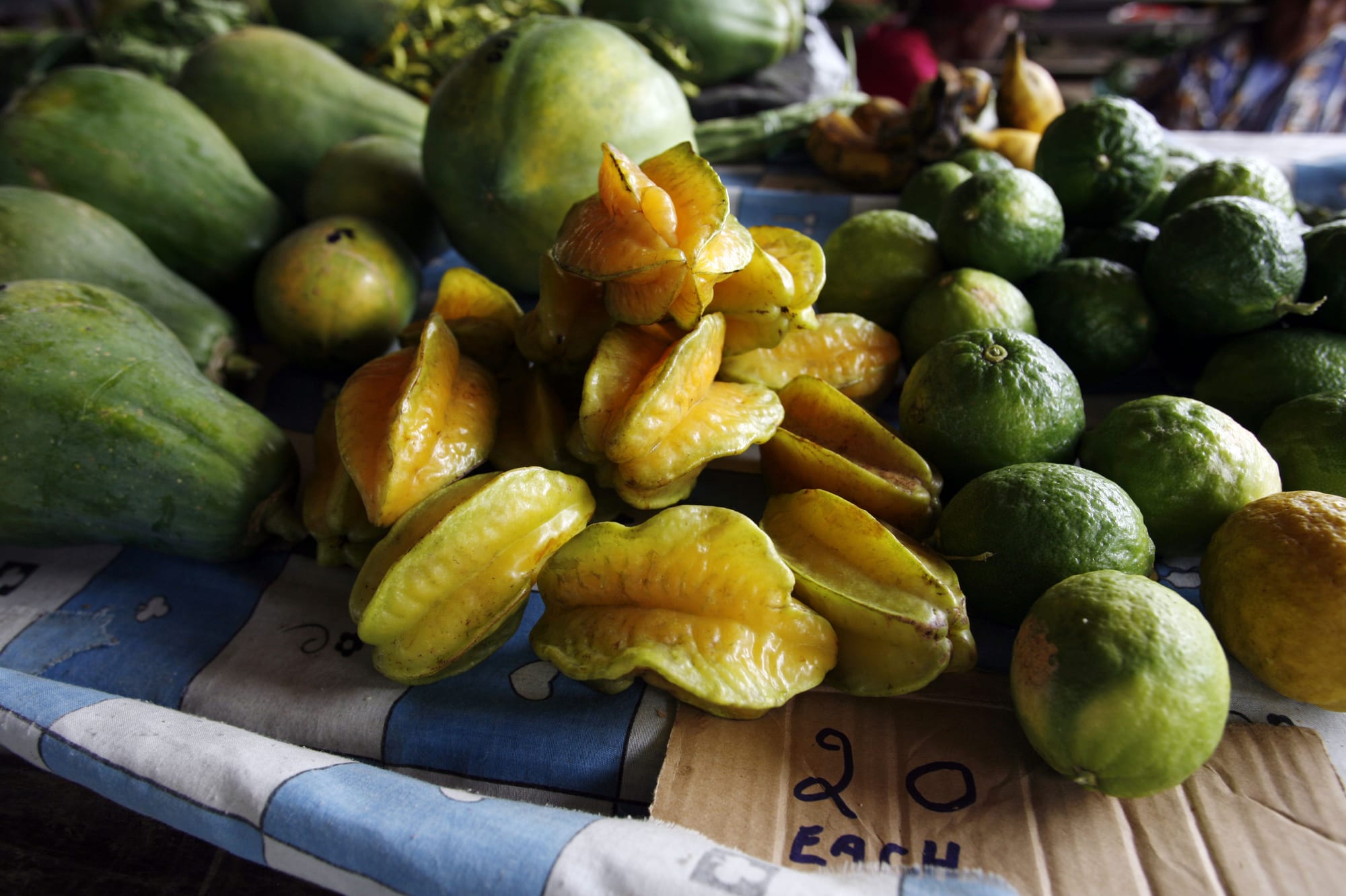 A close-up of tropical produce for sale at a market stall, including star fruit, papaya, limes and root vegetables