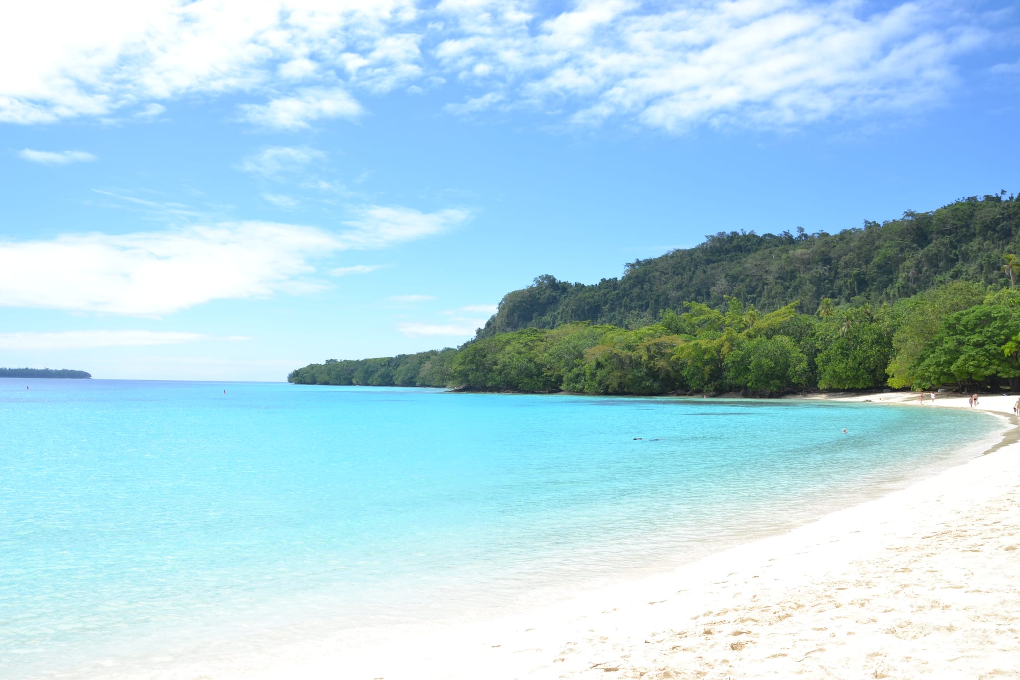 A curving white-sand beach with turquoise water and a forested headland
