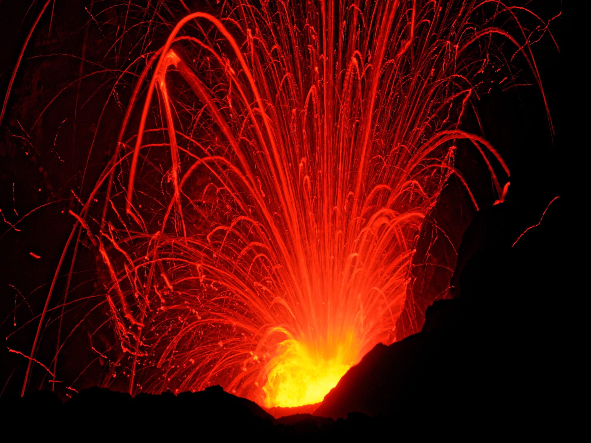 Glowing lava trails erupting from a volcanic crater at night