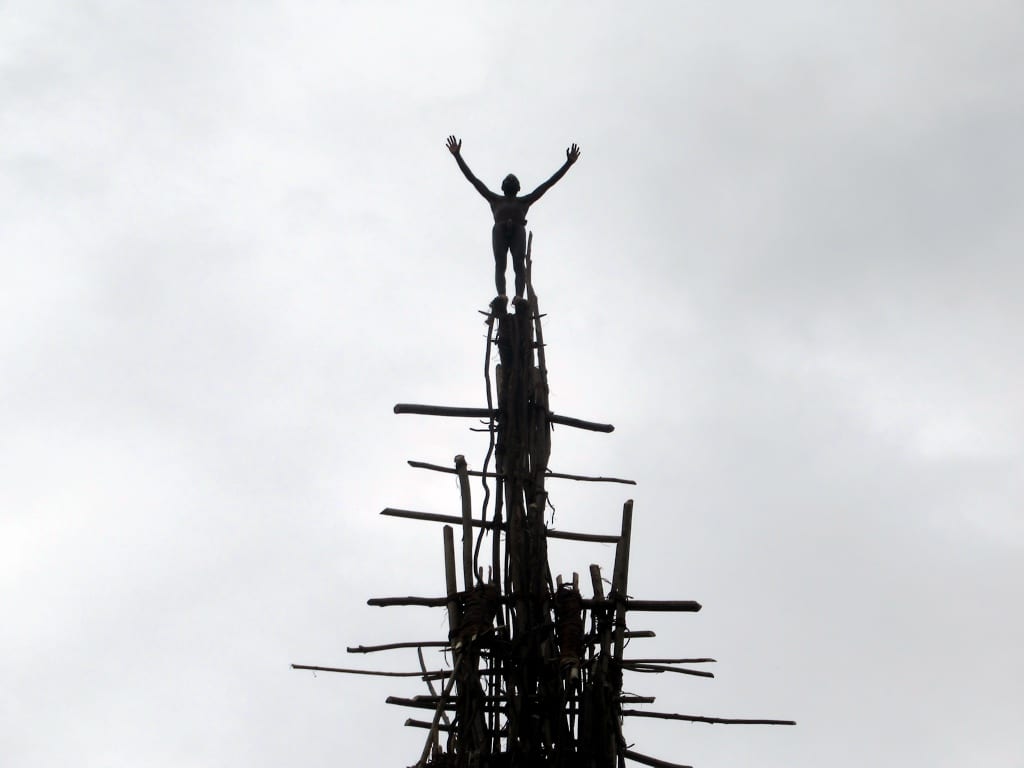 A man diving headfirst from a tall wooden tower with vines tied to his ankles