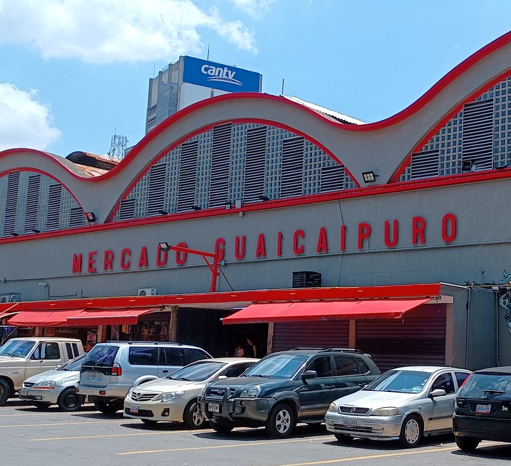 The wave-roofed exterior of the Mercado Guaicaipuro market building in Caracas, with cars parked outside