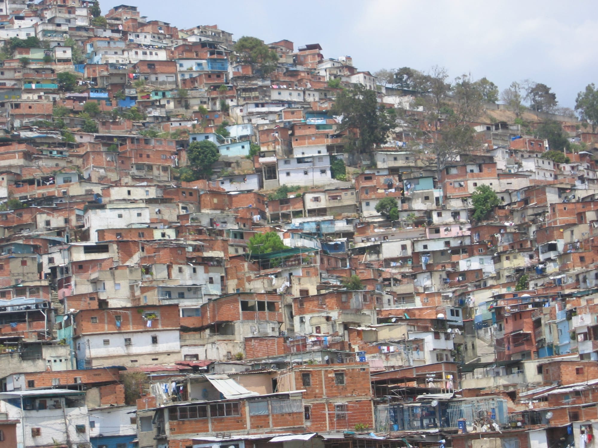 Dense, self-built housing in reds, whites and blues covering a steep hillside above Caracas