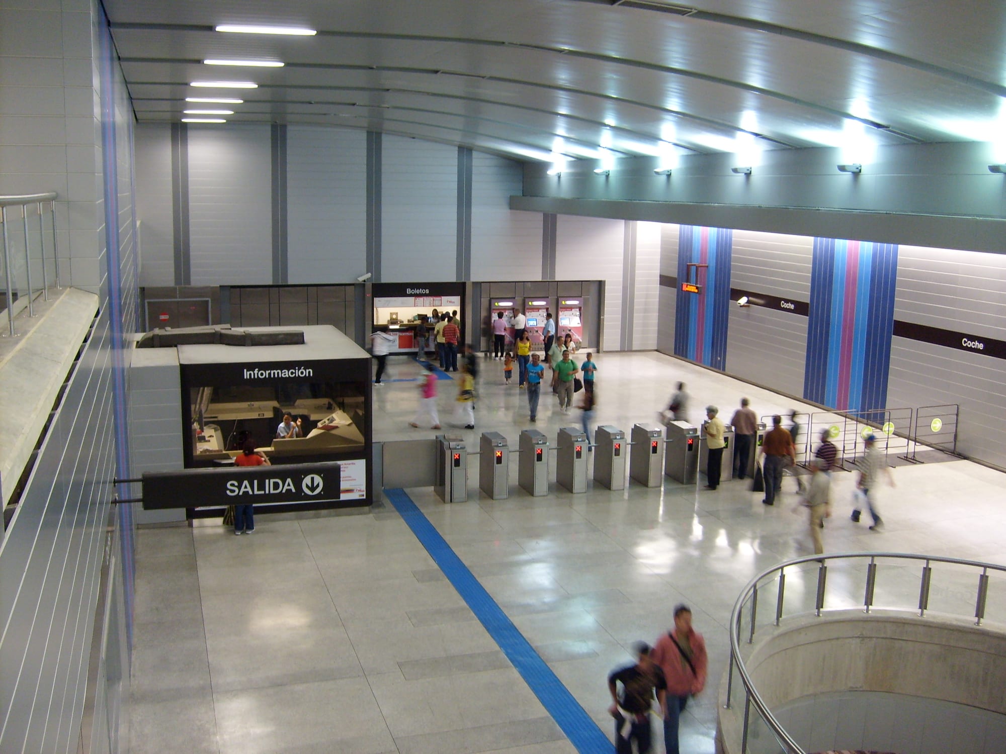Commuters walking through the ticket hall and turnstiles of a Caracas Metro station under fluorescent light