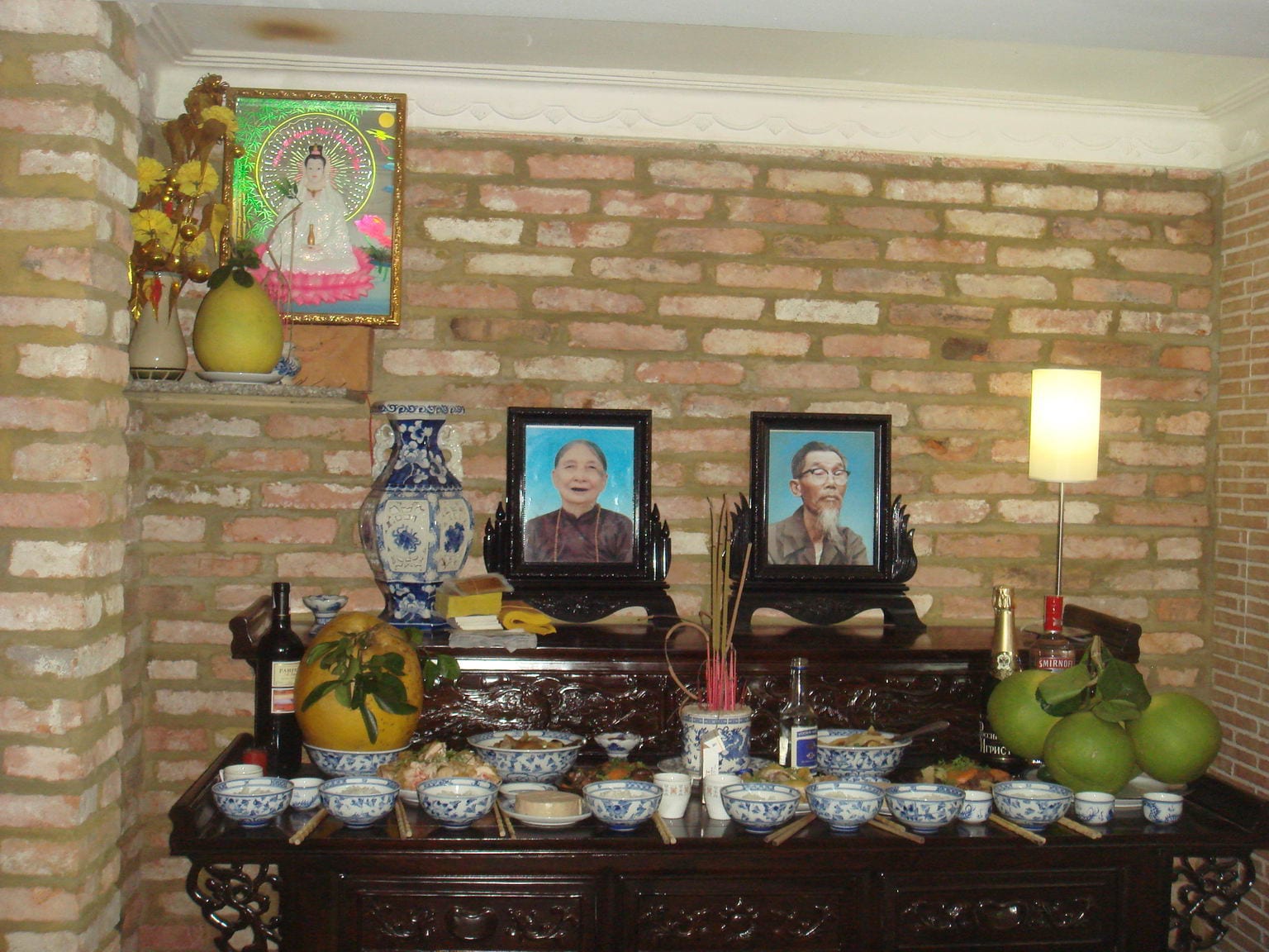 A Vietnamese household ancestor altar with framed photographs, incense, fruit and bowls of food laid out on a wooden cabinet
