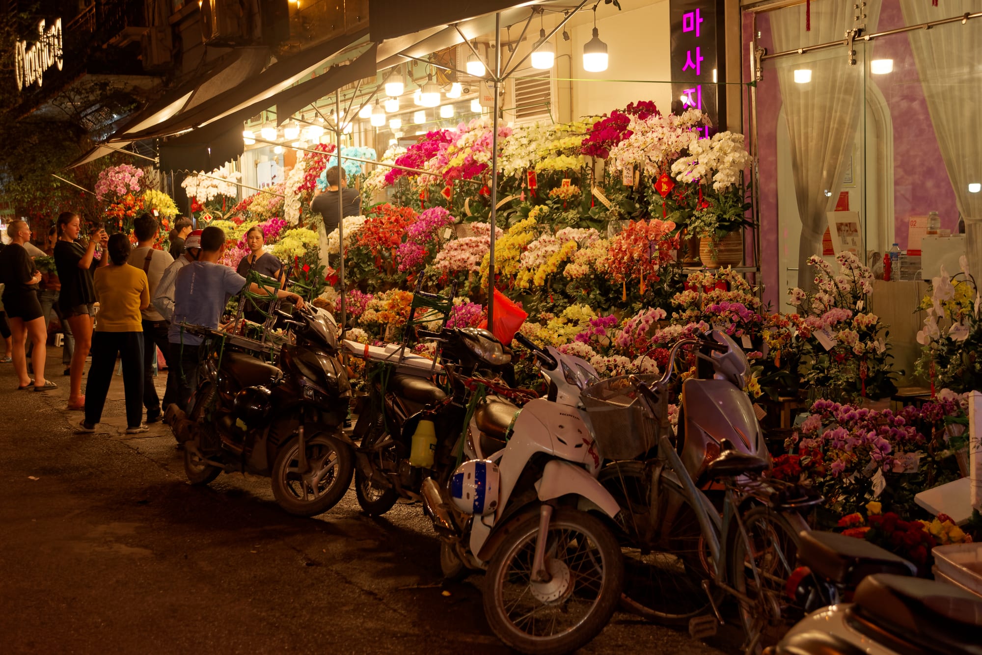 Motorbikes parked outside a flower shop overflowing with colourful blooms at night