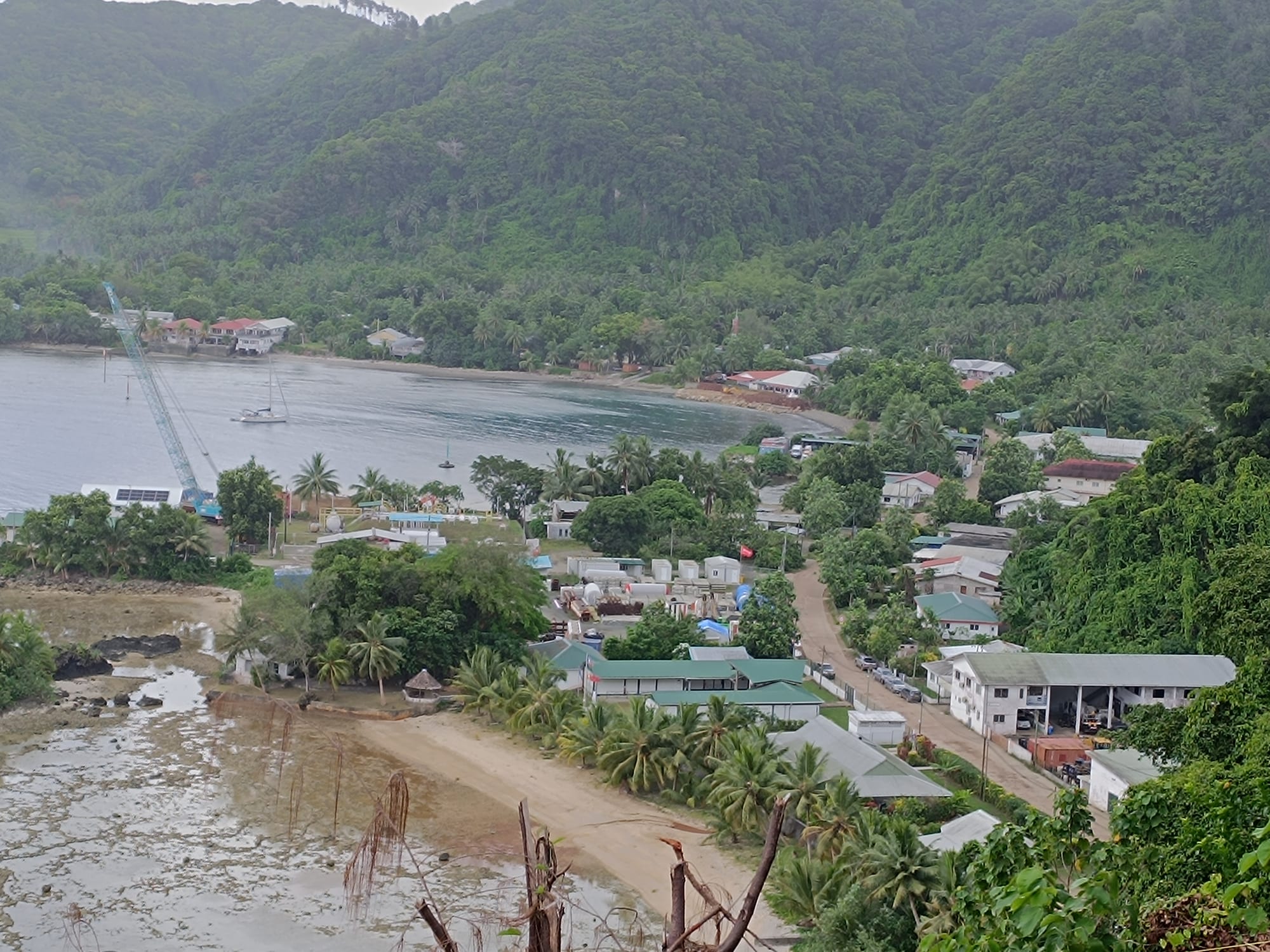 An aerial view of Leava village on Futuna, houses and palm trees along a curving bay with green hills behind