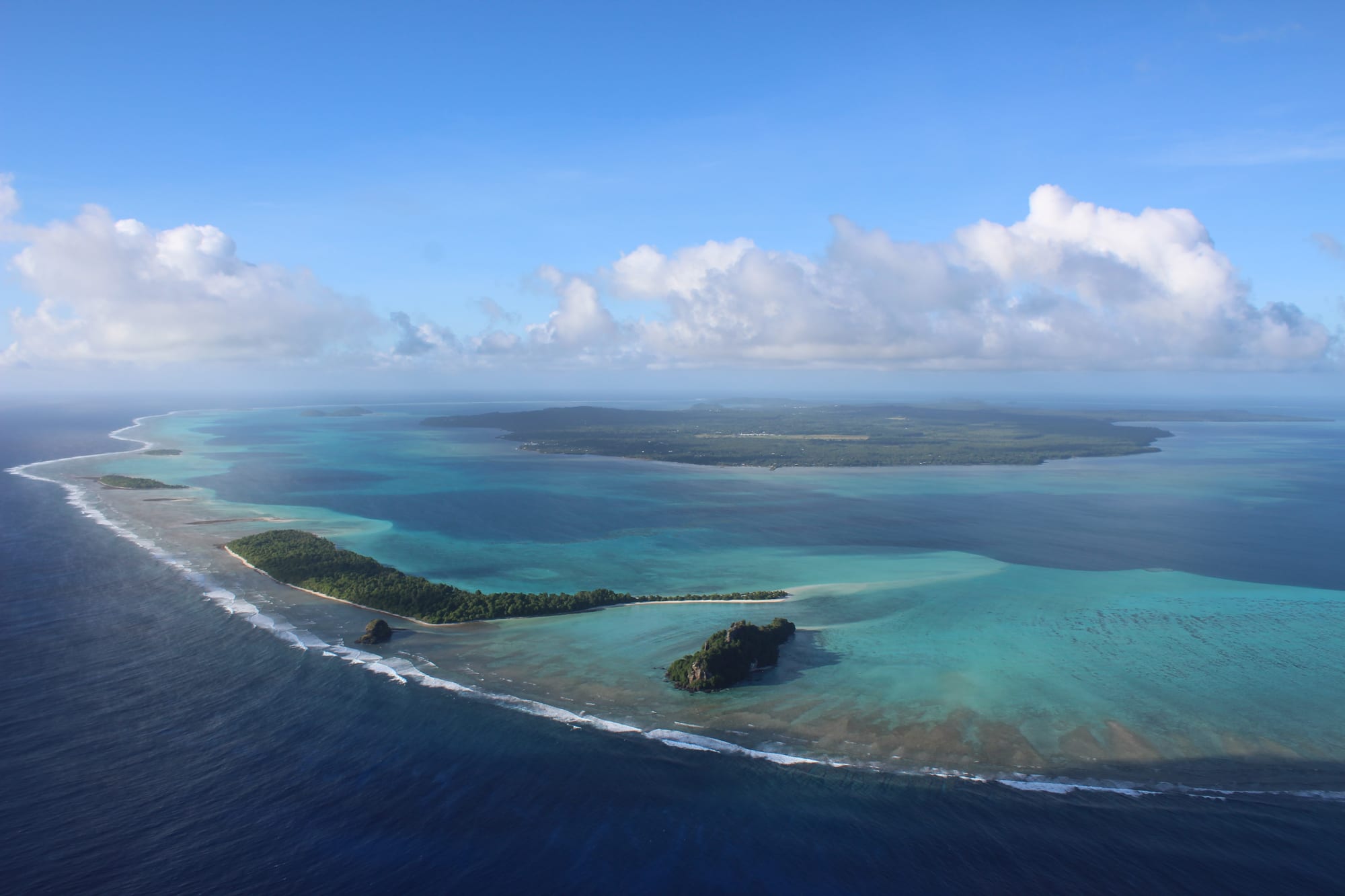 An aerial view of a green tropical island surrounded by a lagoon and reef