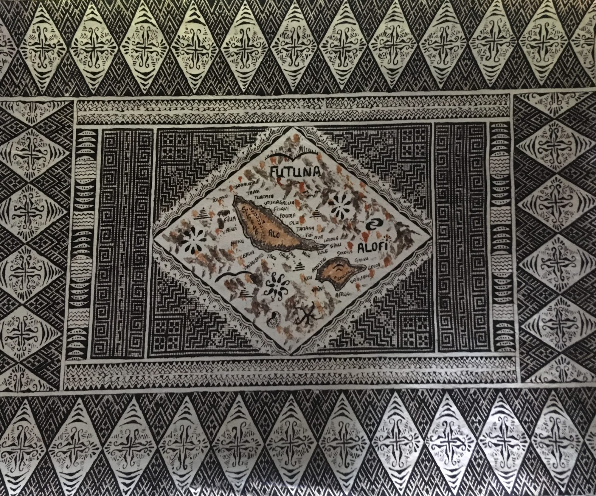 A large tapa cloth painted in black and cream with bands of diamonds, zigzags and geometric patterns framing a central map of the islands of Futuna and Alofi