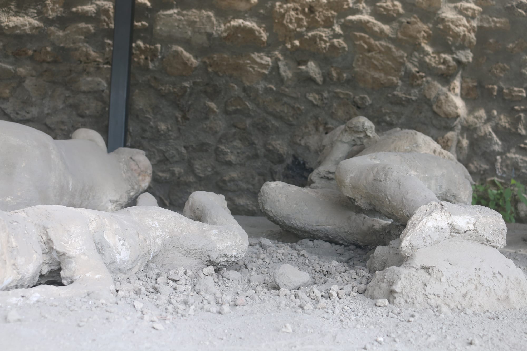 Grey plaster figures of people lying curled on the ground in front of a rough stone wall