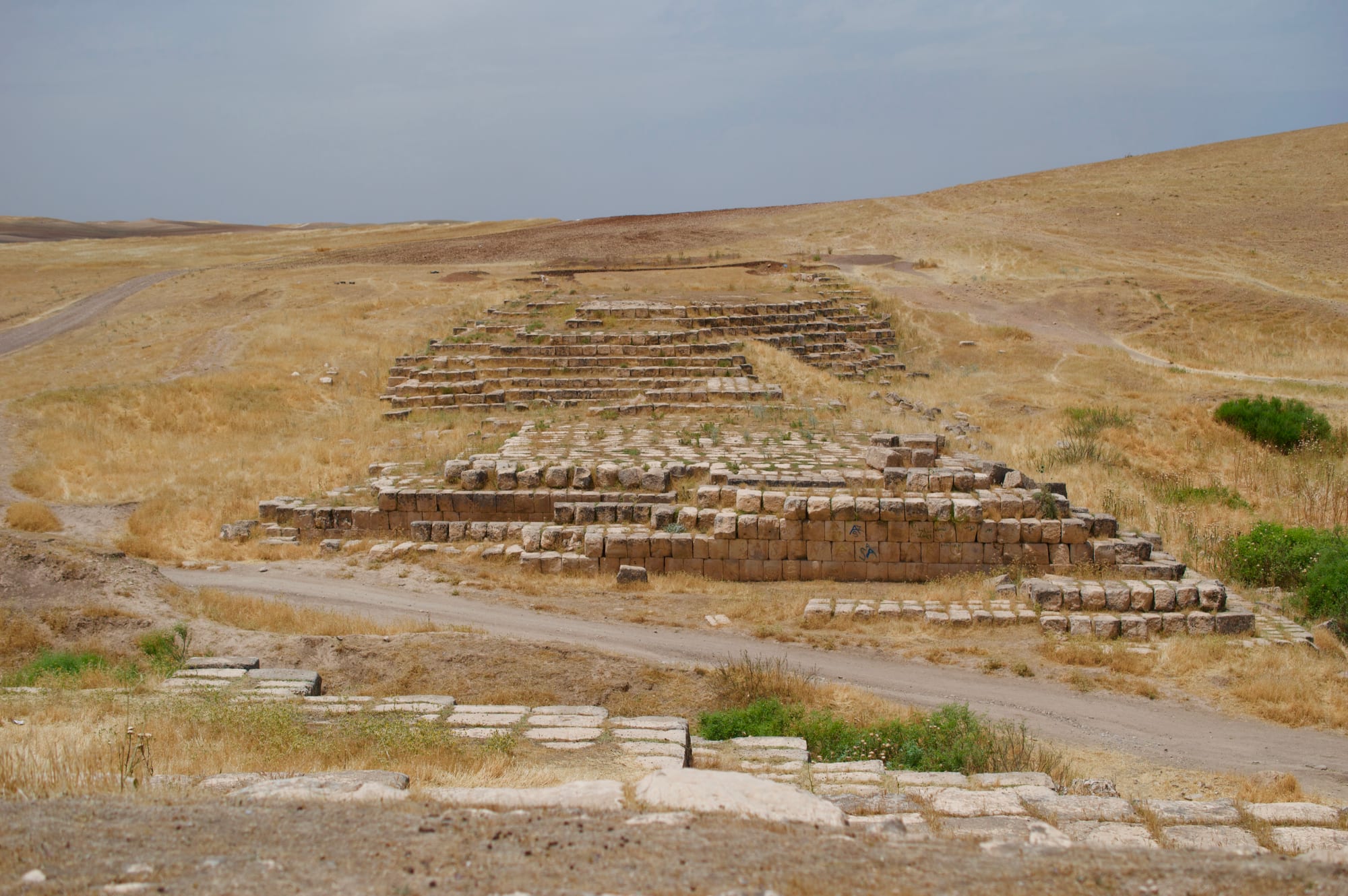 Rows of large cut limestone blocks forming the remains of a raised channel across dry grassy hills