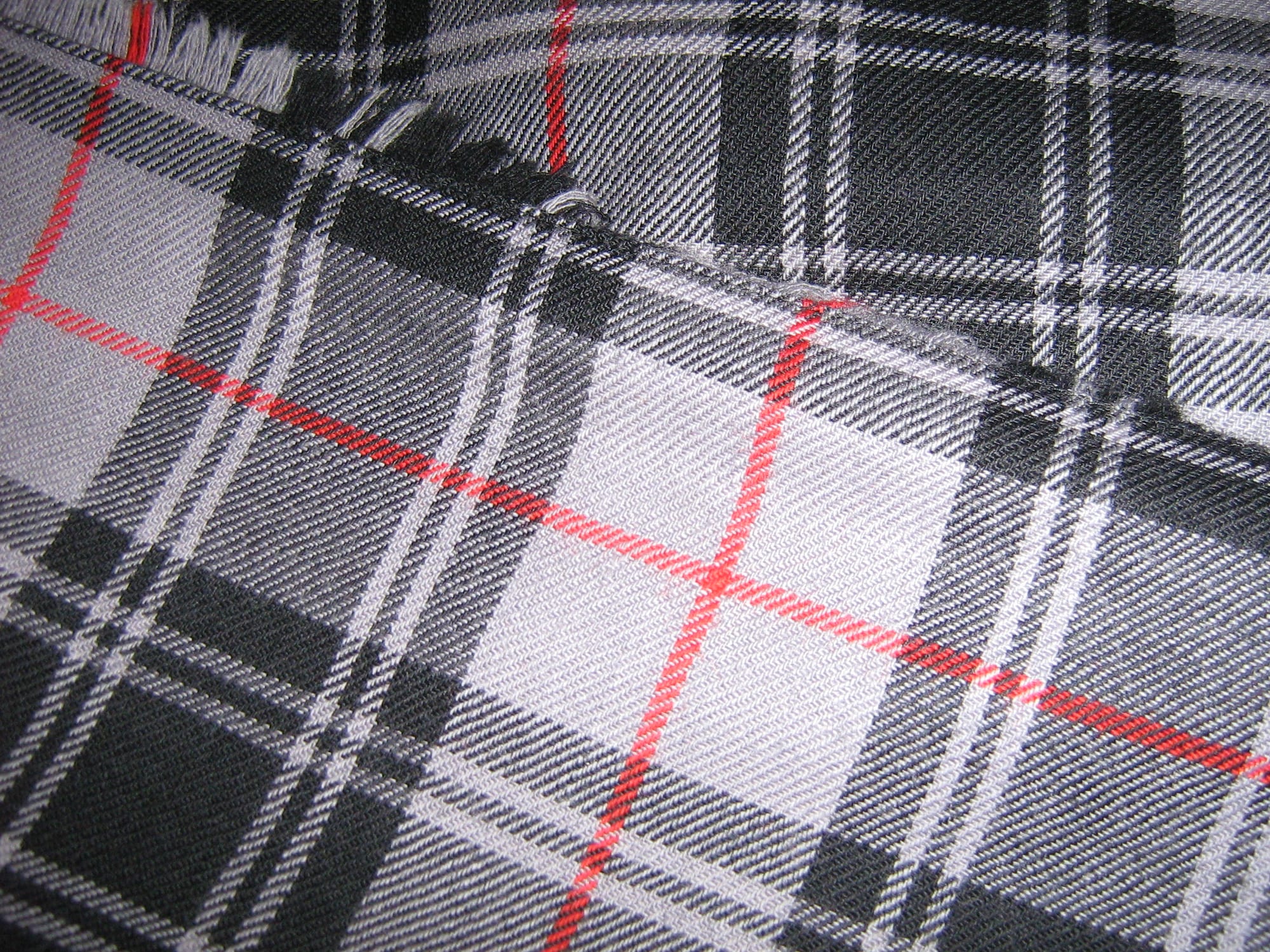 Close-up of grey, black and white checked woollen cloth crossed by thin red lines, with the fine diagonal ribs of a twill weave visible