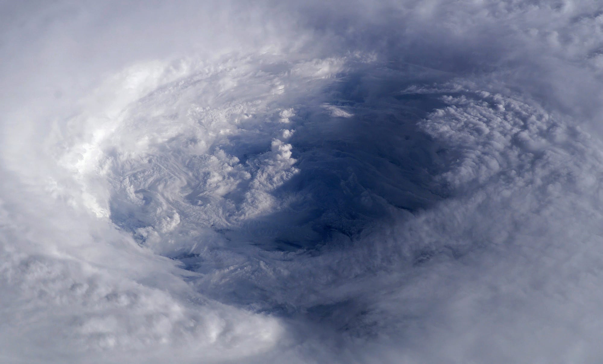 Looking down into the eye of a vast storm, a deep bowl of clear air ringed by towering walls of white cloud