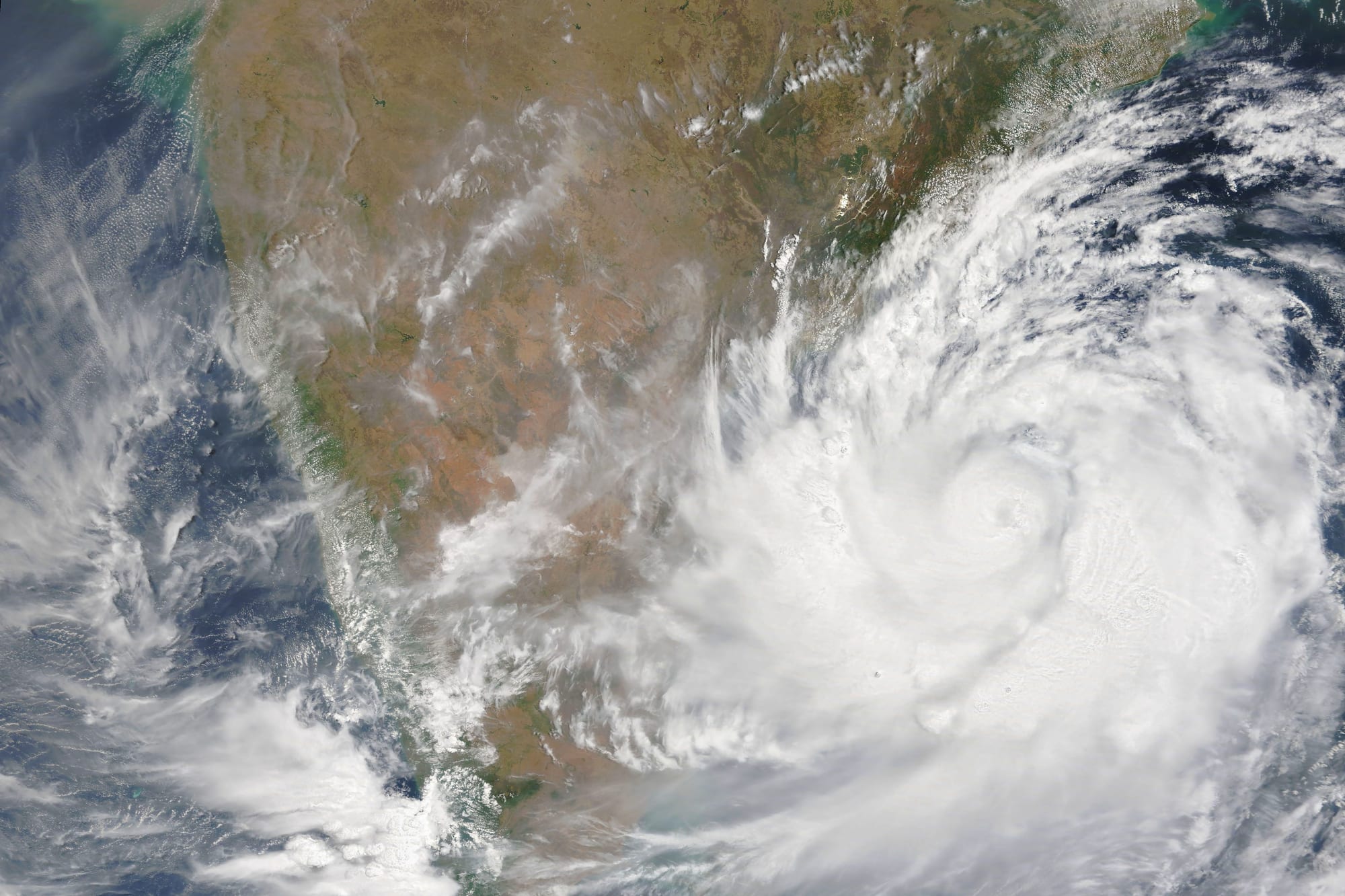 A satellite view of a large white spiral of cloud over the sea, reaching onto the brown land of southern India