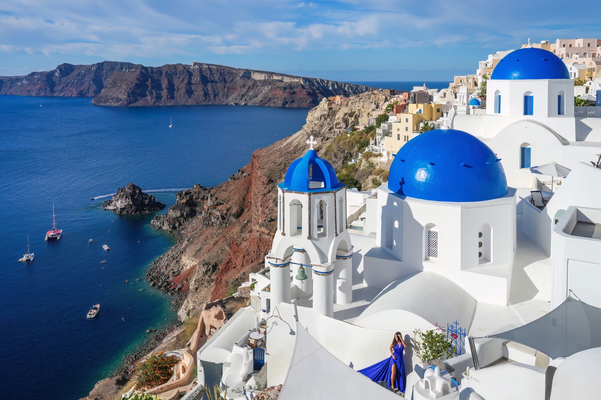 Bright blue church domes and a white bell tower on whitewashed buildings at the edge of a cliff above a deep blue sea