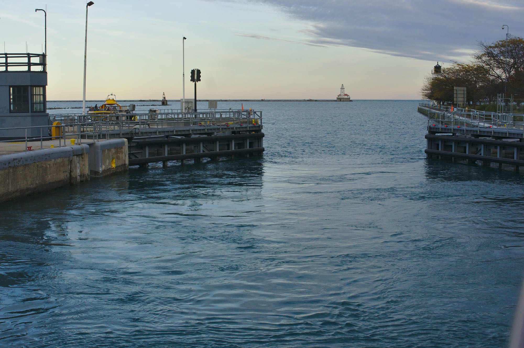 Open lock gates on either side of a channel looking out to a calm lake, with a small lighthouse on a breakwater in the distance