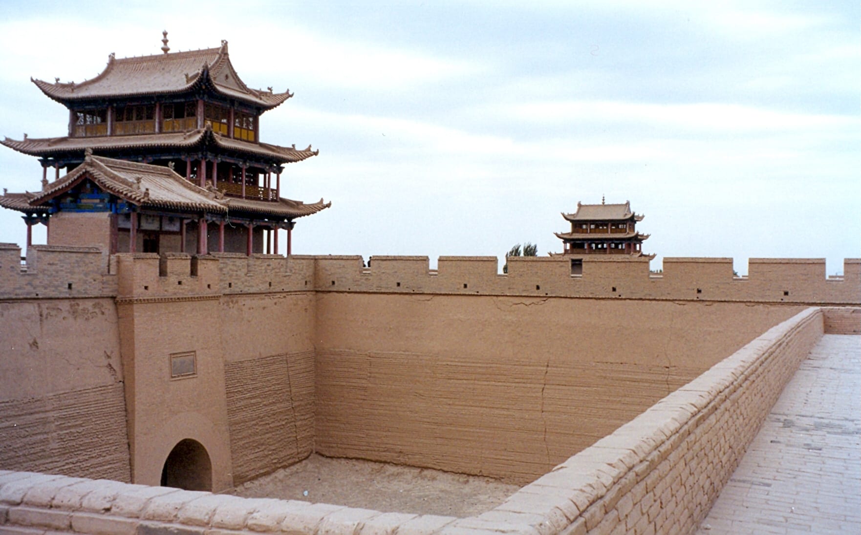 Earth-coloured fortress walls with battlements and an arched gateway, beneath a multi-storey tiled gate tower
