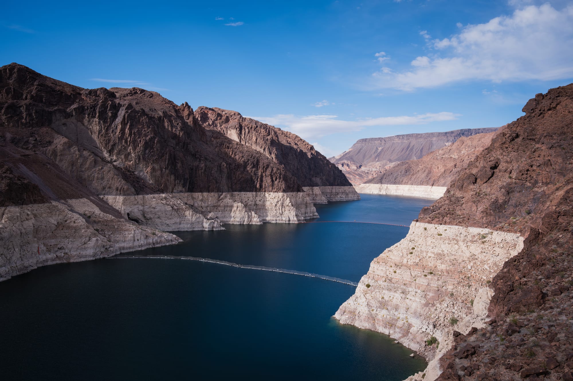 A deep blue reservoir winding between dark rocky canyon walls, with a thick band of white mineral staining above the waterline