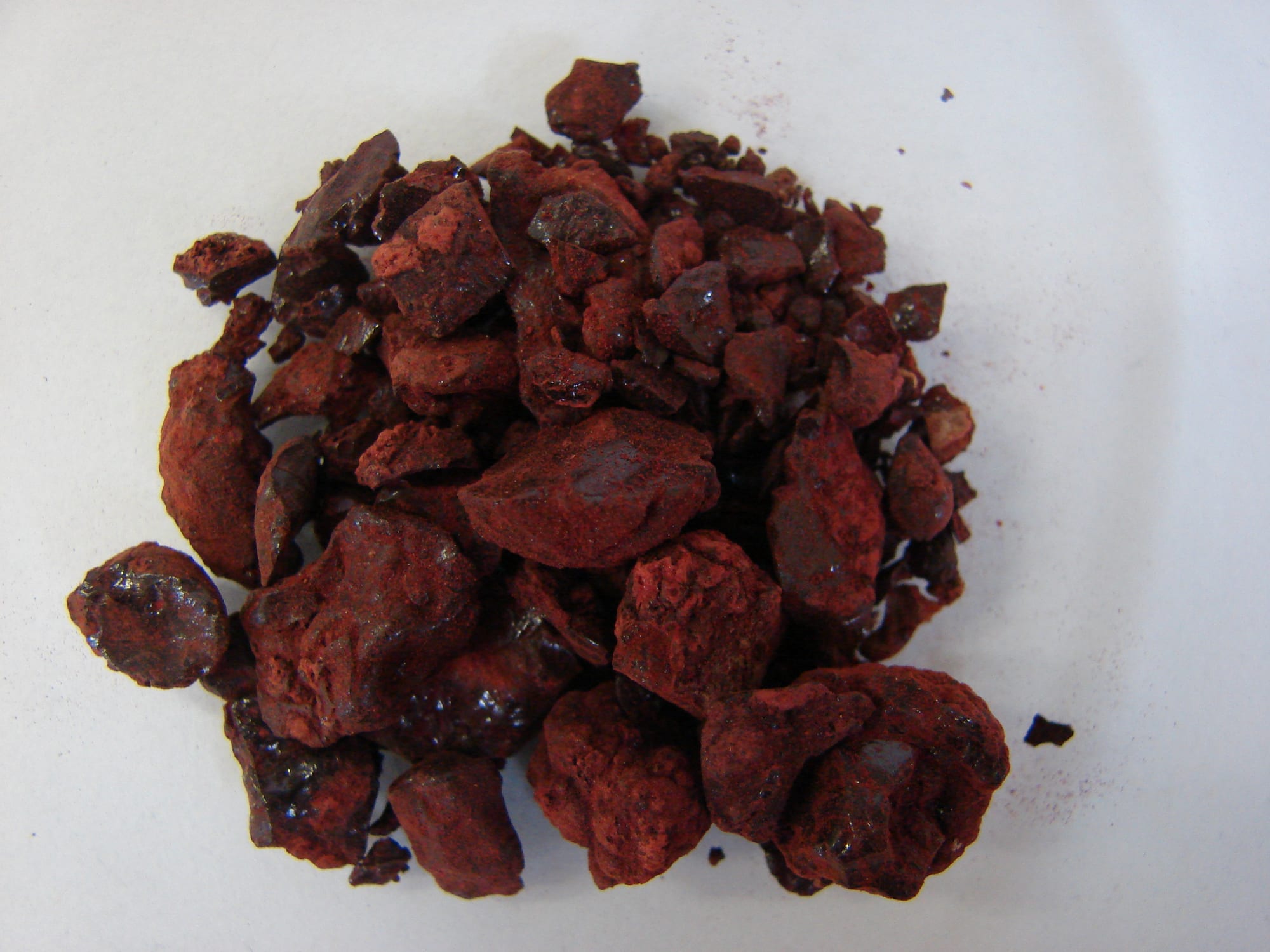 A small heap of dark red, irregular lumps of resin dusted with crimson powder on a white surface
